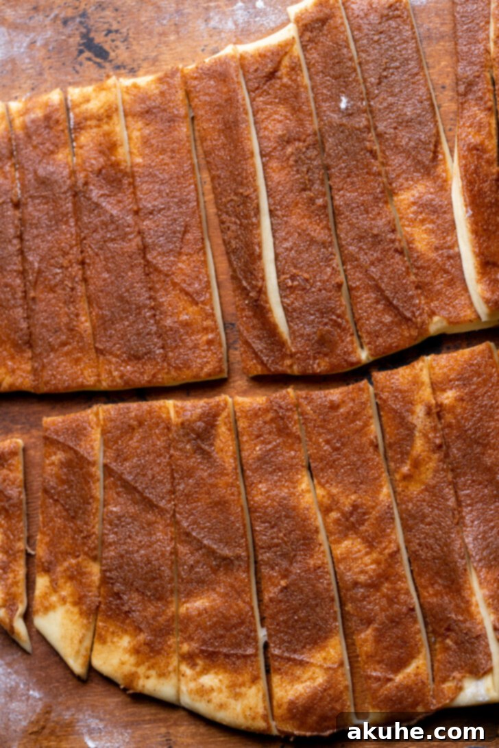 Dough cut into strips and being rolled into individual cinnamon rolls.