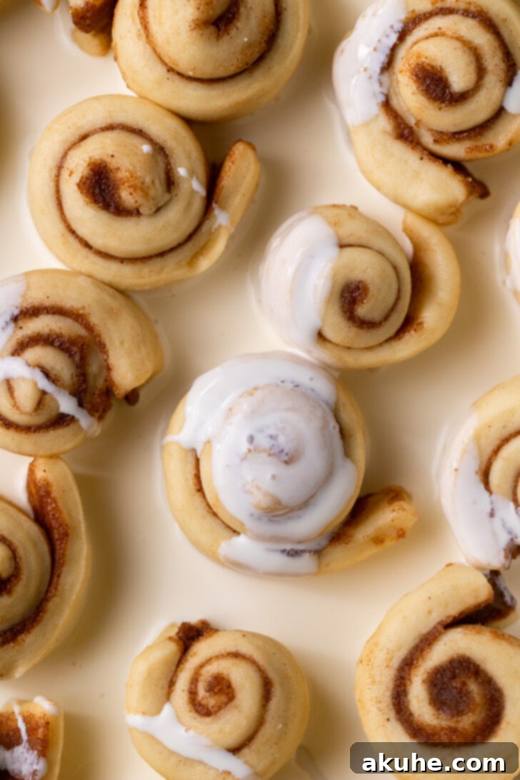 Heavy cream being poured over the unbaked cinnamon rolls in a pan.