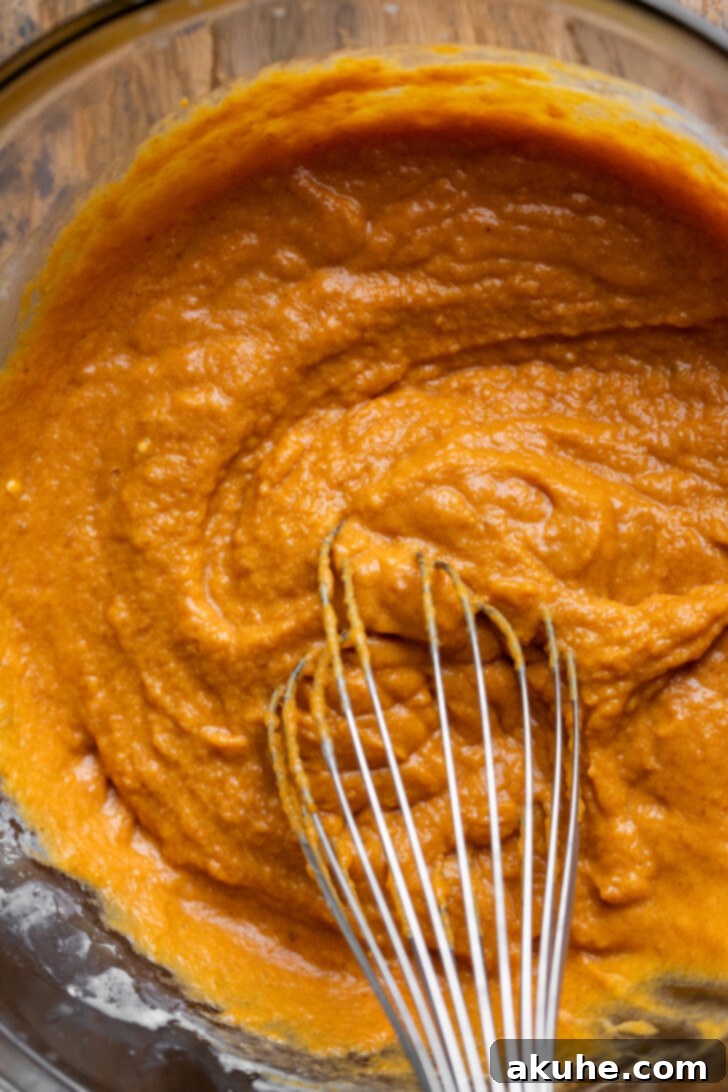 Wet ingredients for pumpkin muffins in a mixing bowl, showcasing the rich orange color of pumpkin puree.