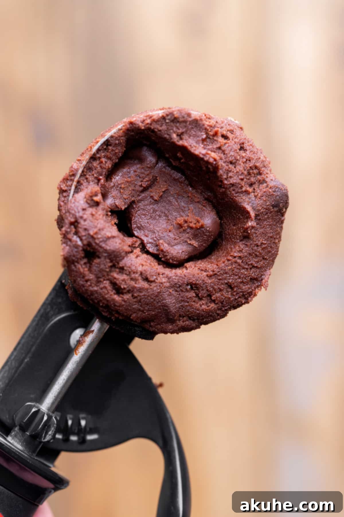 Fudgy Chocolate Delights 7 A dollop of chocolate ganache being carefully placed into an indent in chocolate cookie dough within a cookie scoop.