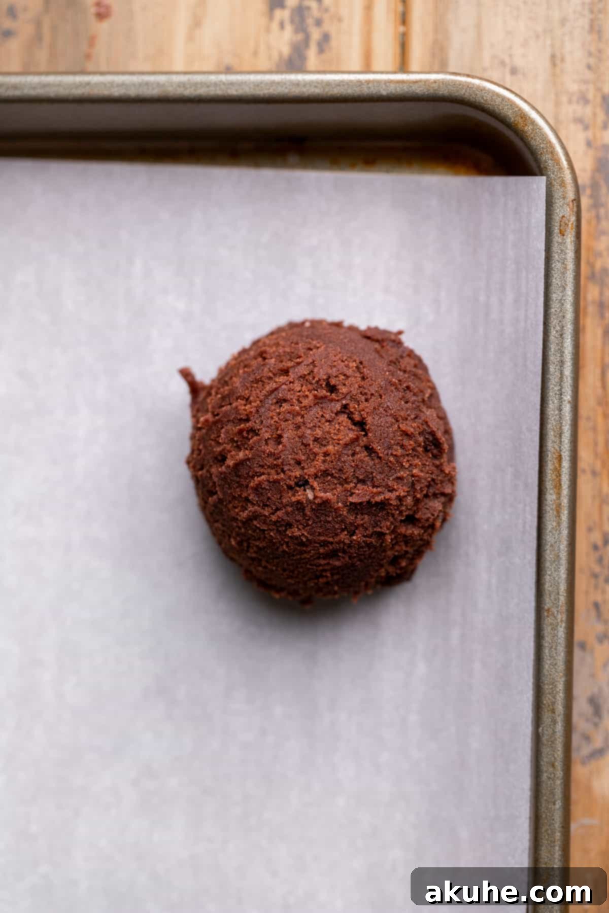 Fudgy Chocolate Delights 8 A perfectly formed chocolate cookie dough ball, with the ganache filling sealed inside, placed on a parchment-lined cookie sheet.