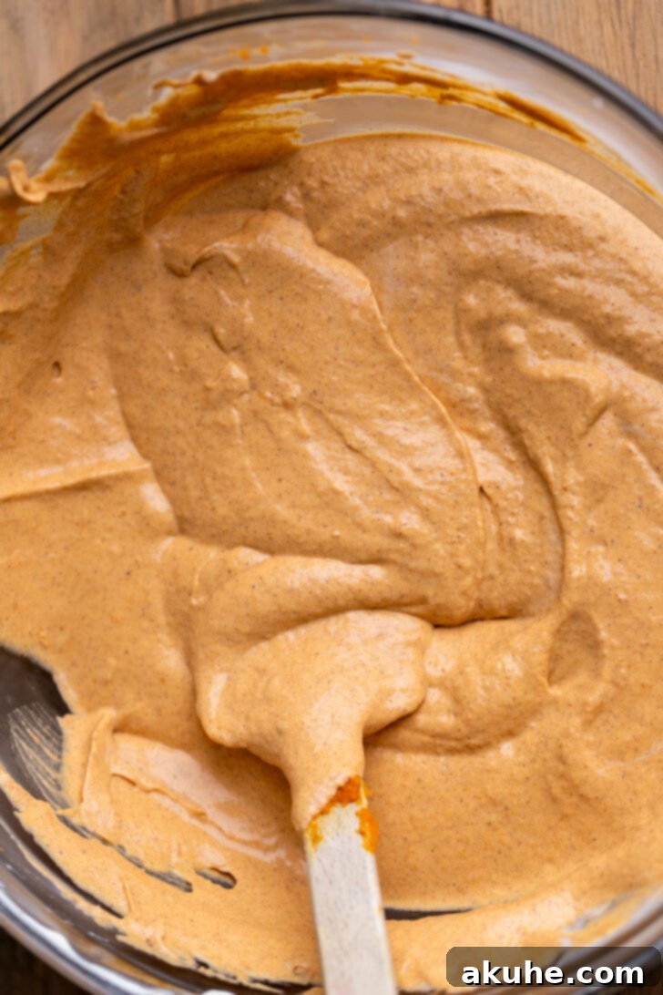 Pumpkin-infused cheesecake batter in a bowl, showing its warm orange hue.