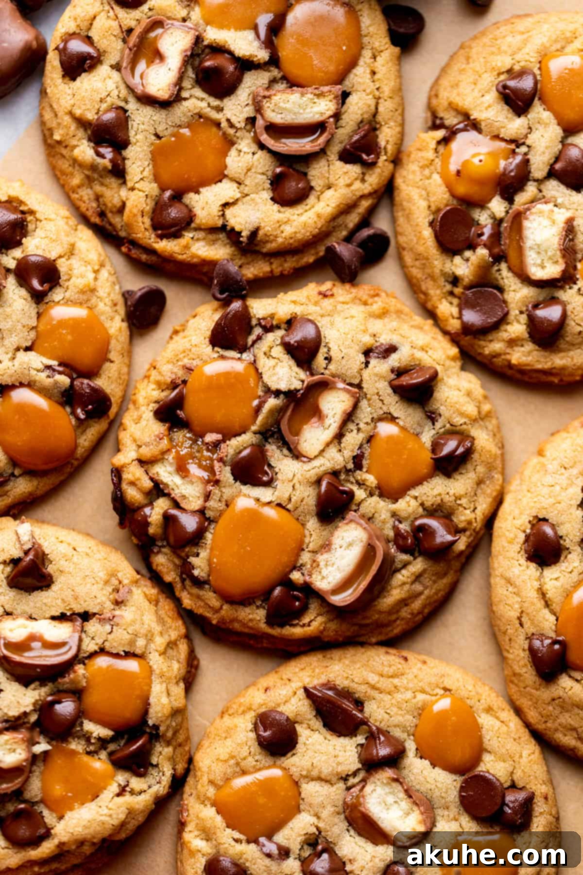 Freshly baked Twix cookies cooling on parchment paper, showcasing their golden edges and gooey caramel tops.
