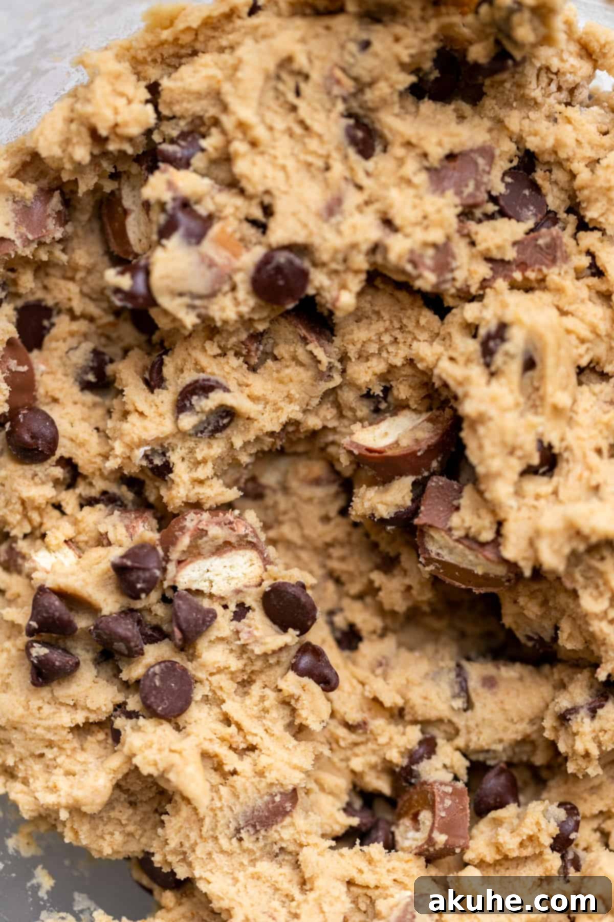Cookie dough with chocolate chips and Twix pieces in a glass bowl.