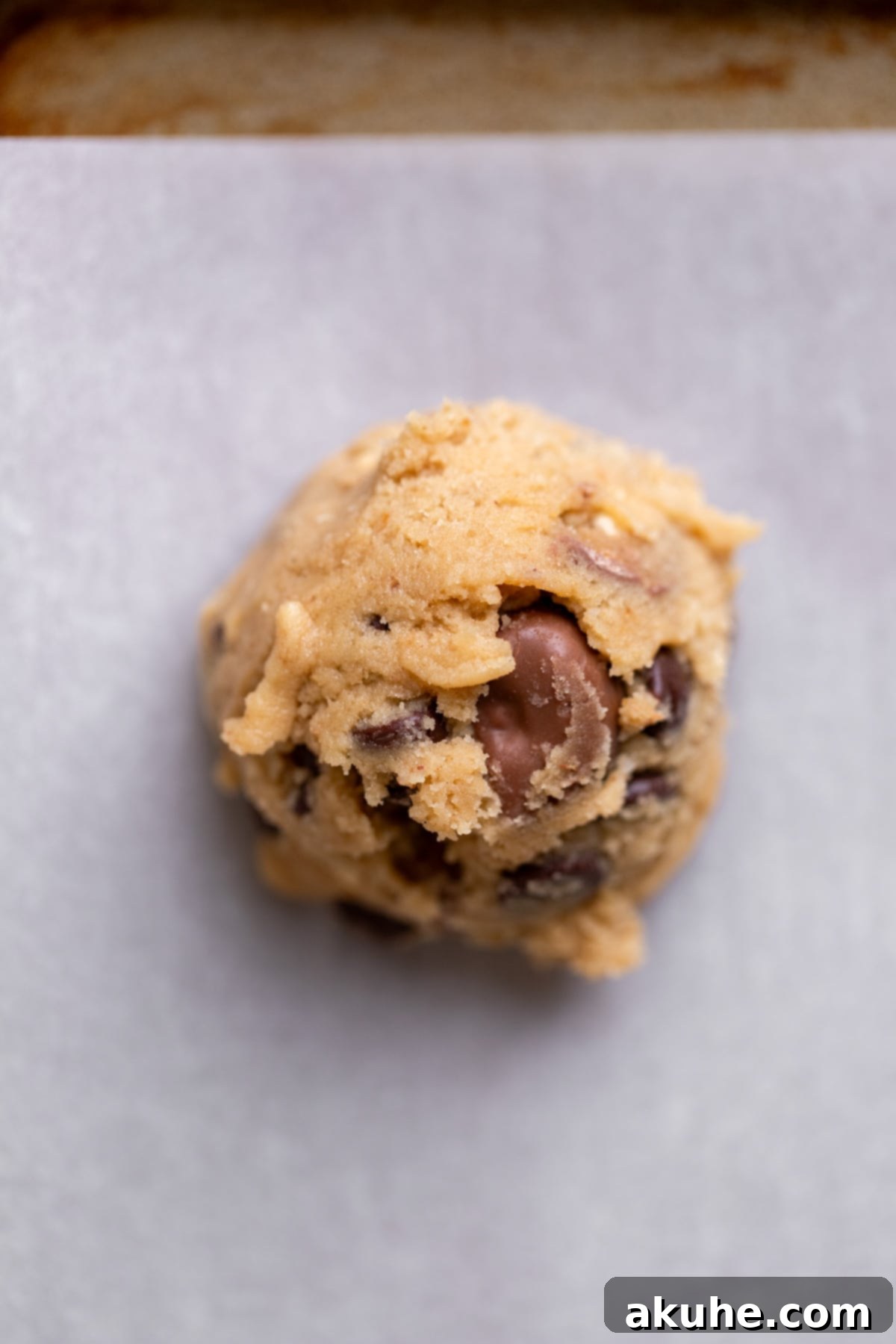 A perfectly scooped cookie dough ball ready for baking on a parchment-lined cookie sheet.