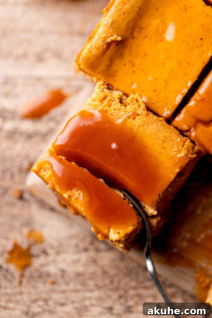Spiced Pumpkin Caramel Cheesecake Bars 8 A fork piercing into a caramel pumpkin cheesecake bar, revealing its soft, creamy interior and delicious layers.
