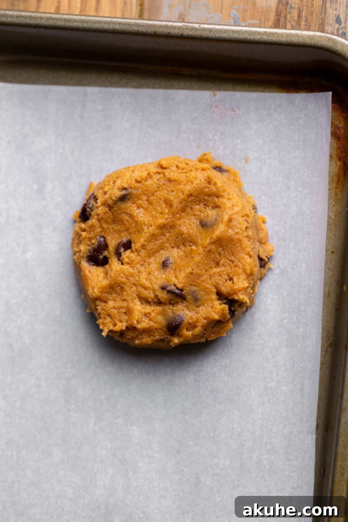 Spiced Pumpkin Chocolate Chip Cookies 6 A perfectly portioned and slightly flattened cookie dough ball resting on a parchment-lined cookie sheet, ready for baking.