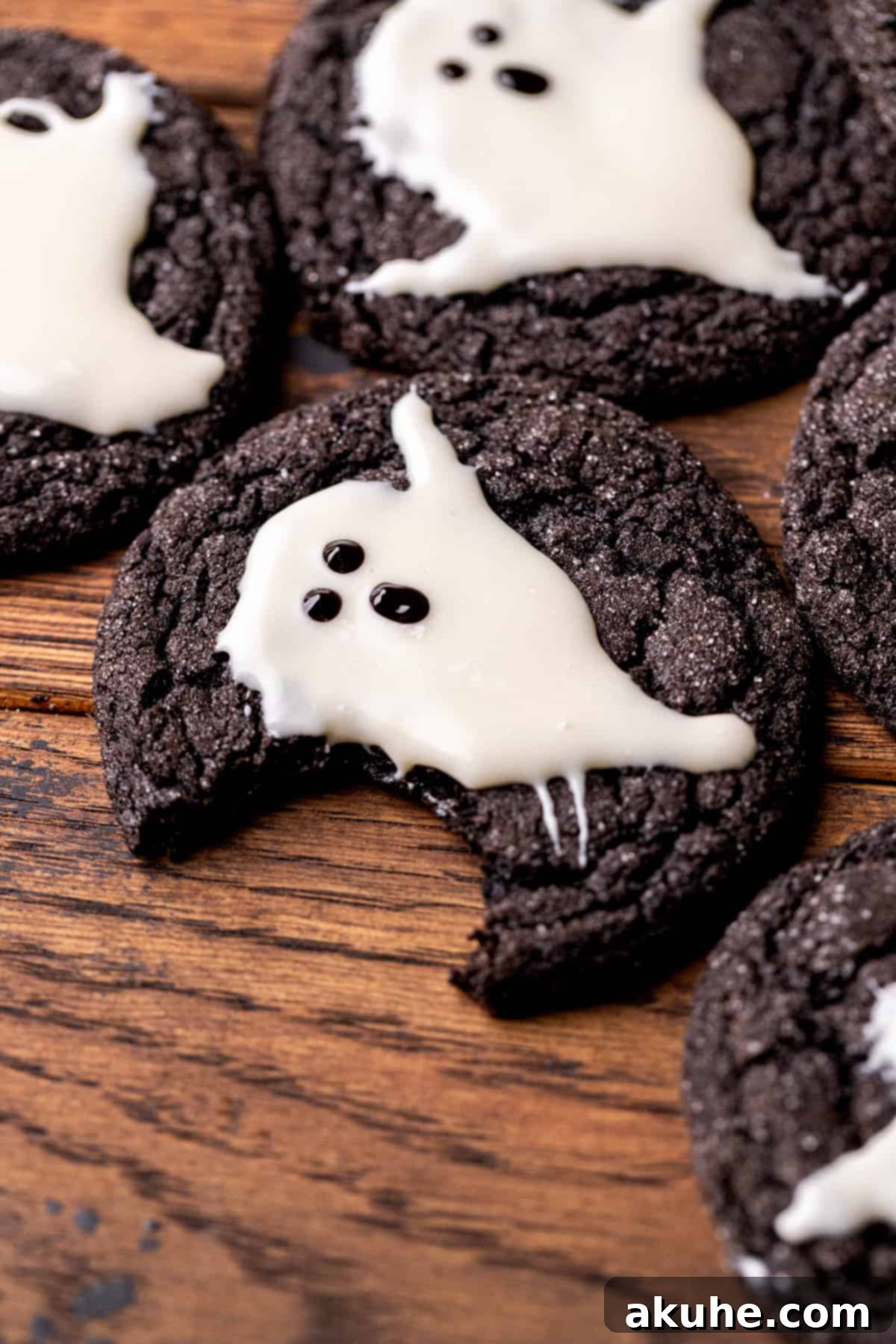 A black cocoa ghost cookie with a bite taken out, revealing its chewy dark interior and the sweet white chocolate ghost topping.