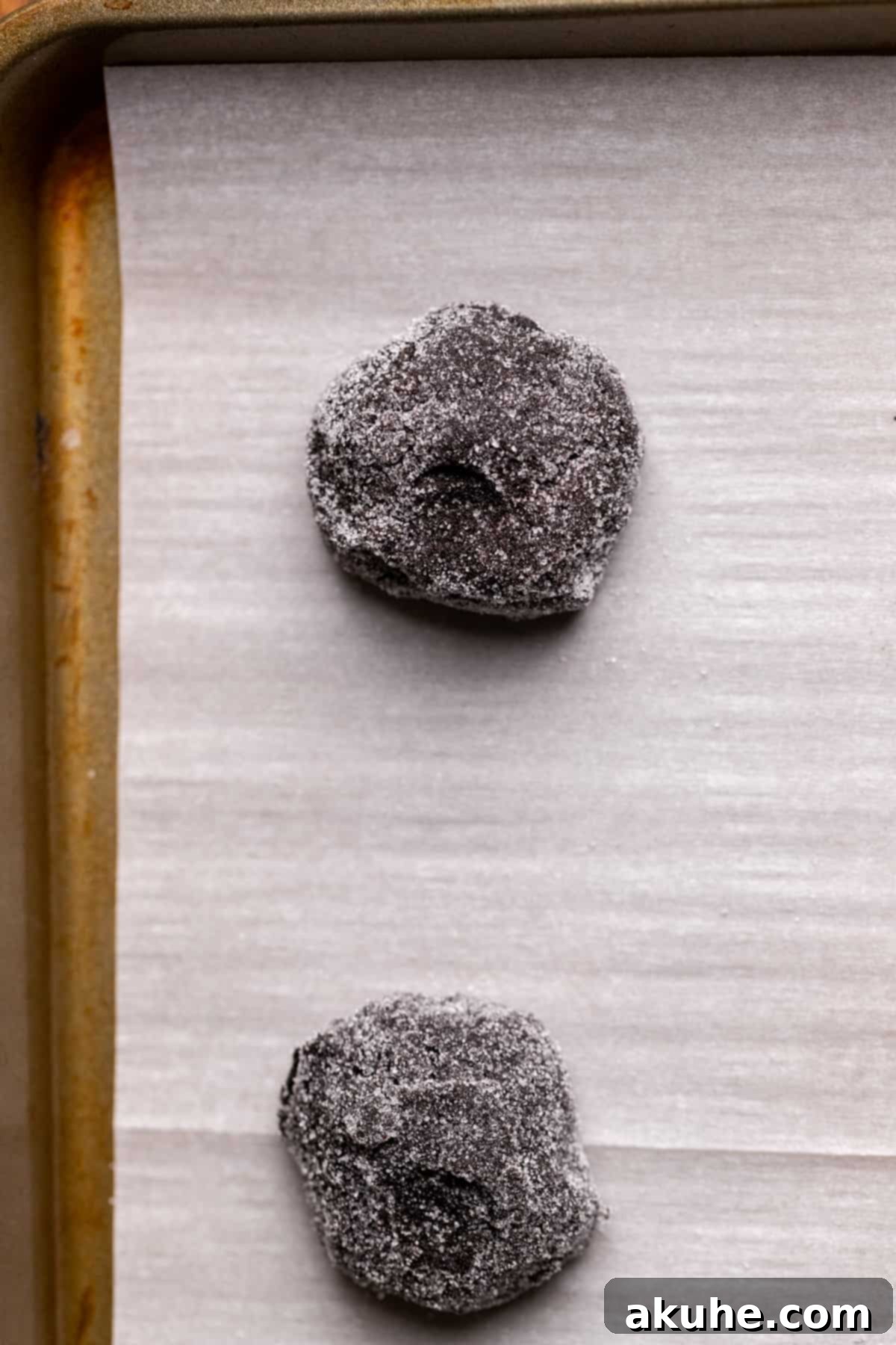 Multiple cookie dough balls, perfectly rolled in sugar, arranged on a parchment-lined cookie sheet, ready for baking.