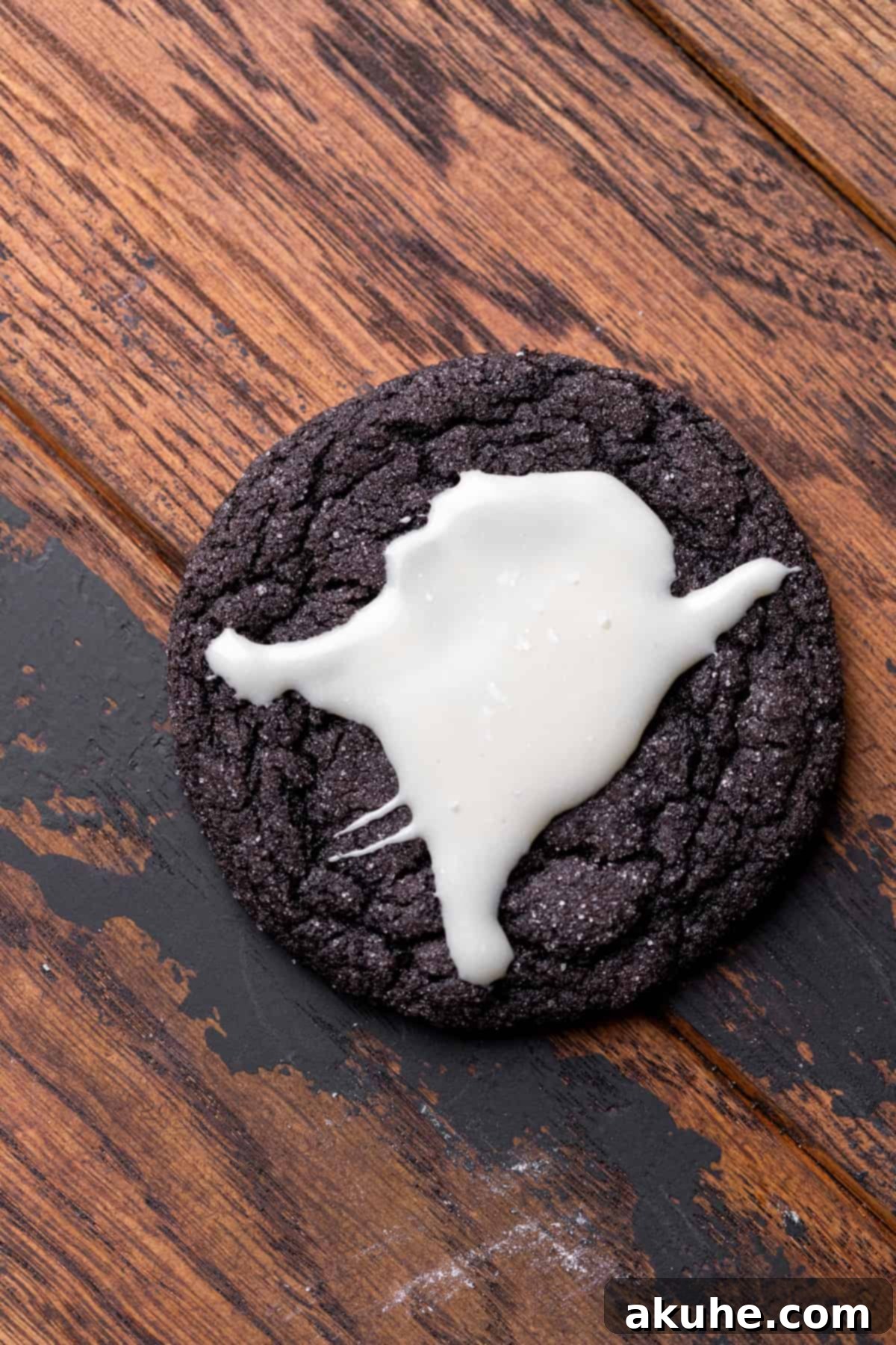 A close-up of a finished black cocoa ghost cookie with its white chocolate ghost topping and black edible gel eyes and mouth.