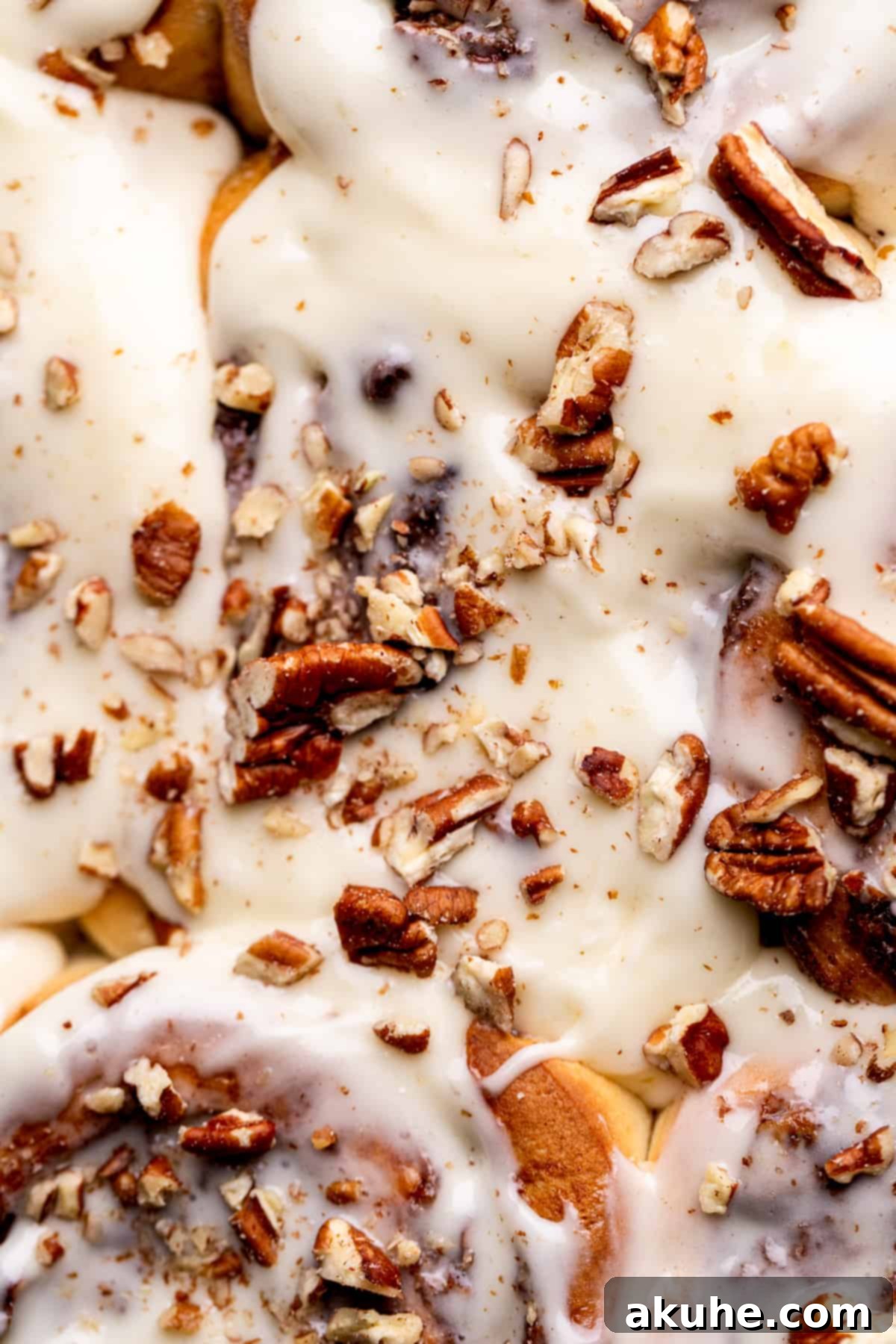 Close-up of a perfectly glazed pecan pie cinnamon roll, showing its soft texture and generous topping.