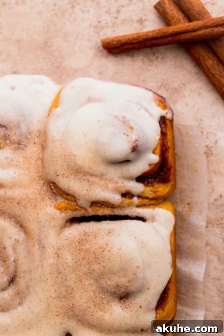 A vibrant top-down view of a baking dish filled with pumpkin cinnamon rolls, fully iced and ready to serve.