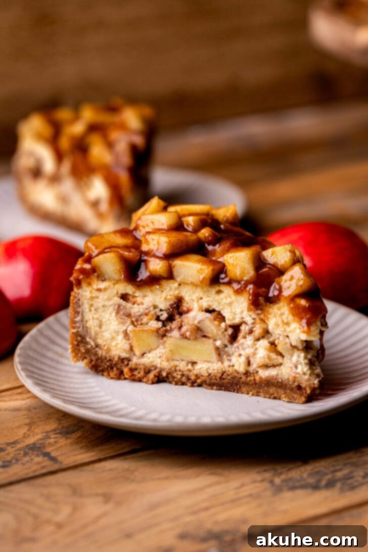 Spiced Apple Pie Cheesecake 2 Side view of a beautifully plated Apple Pie Cheesecake, showcasing its distinct layers of graham cracker crust, creamy cheesecake, and spiced apple filling, topped with more apples.