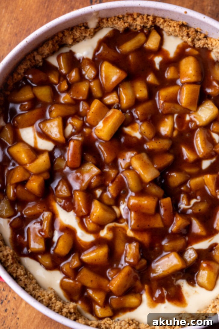 Spiced Apple Pie Cheesecake 6 Spoon dolloping apple pie filling over the first layer of cheesecake batter in a springform pan.