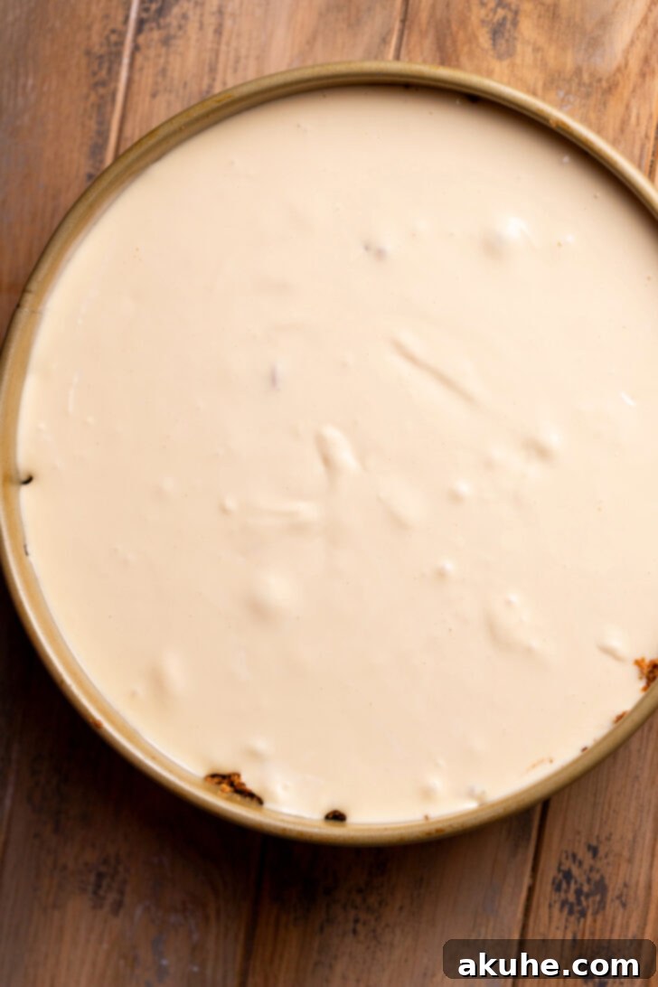 Spiced Apple Pie Cheesecake 7 Cheesecake batter being spread evenly on top of the apple filling layer.