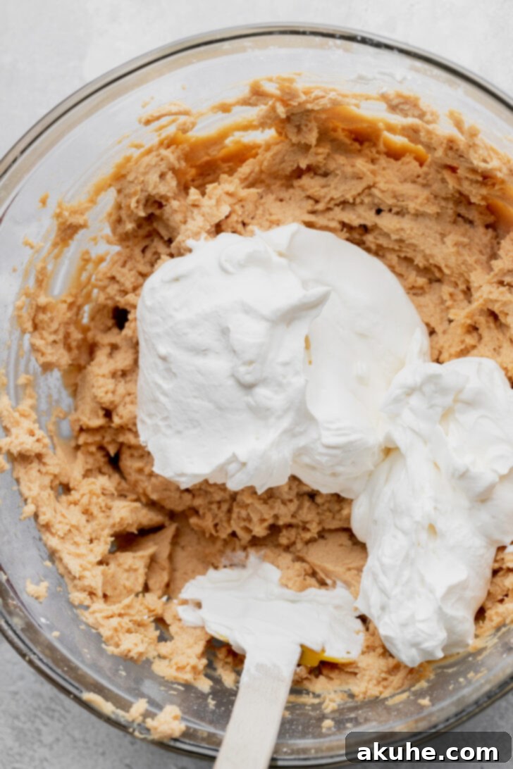 Light and airy whipped cream gently placed on top of the peanut butter batter, ready to be folded in.
