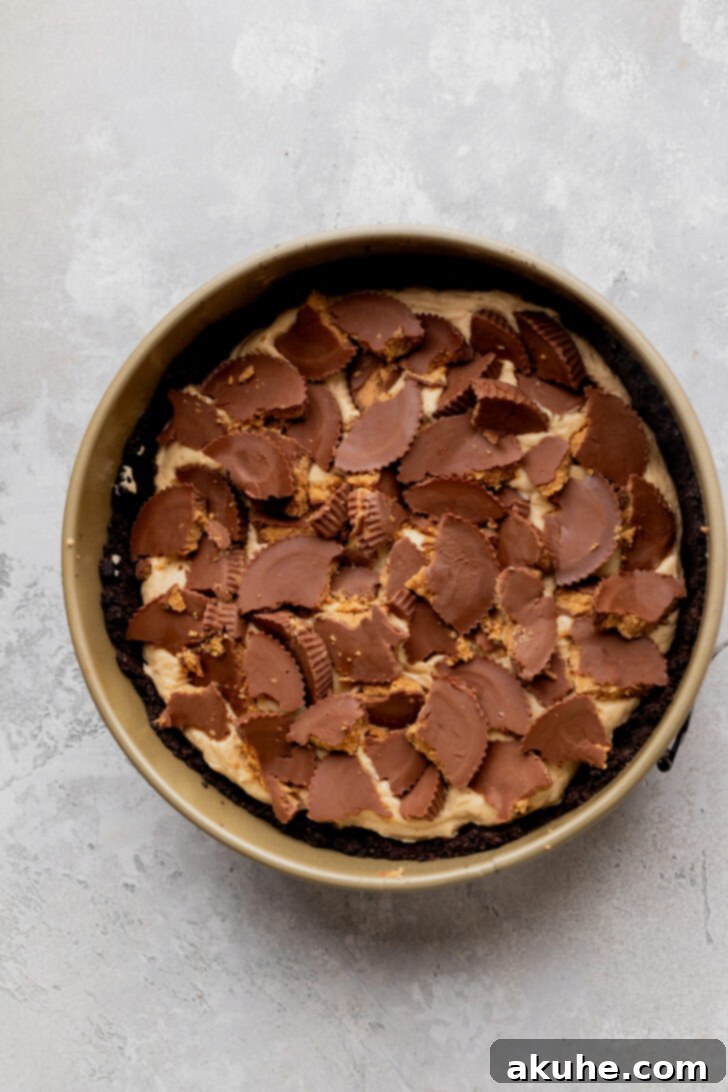 Generous amount of chopped Reese’s peanut butter cups scattered on top of the first layer of peanut butter filling in the pie pan.