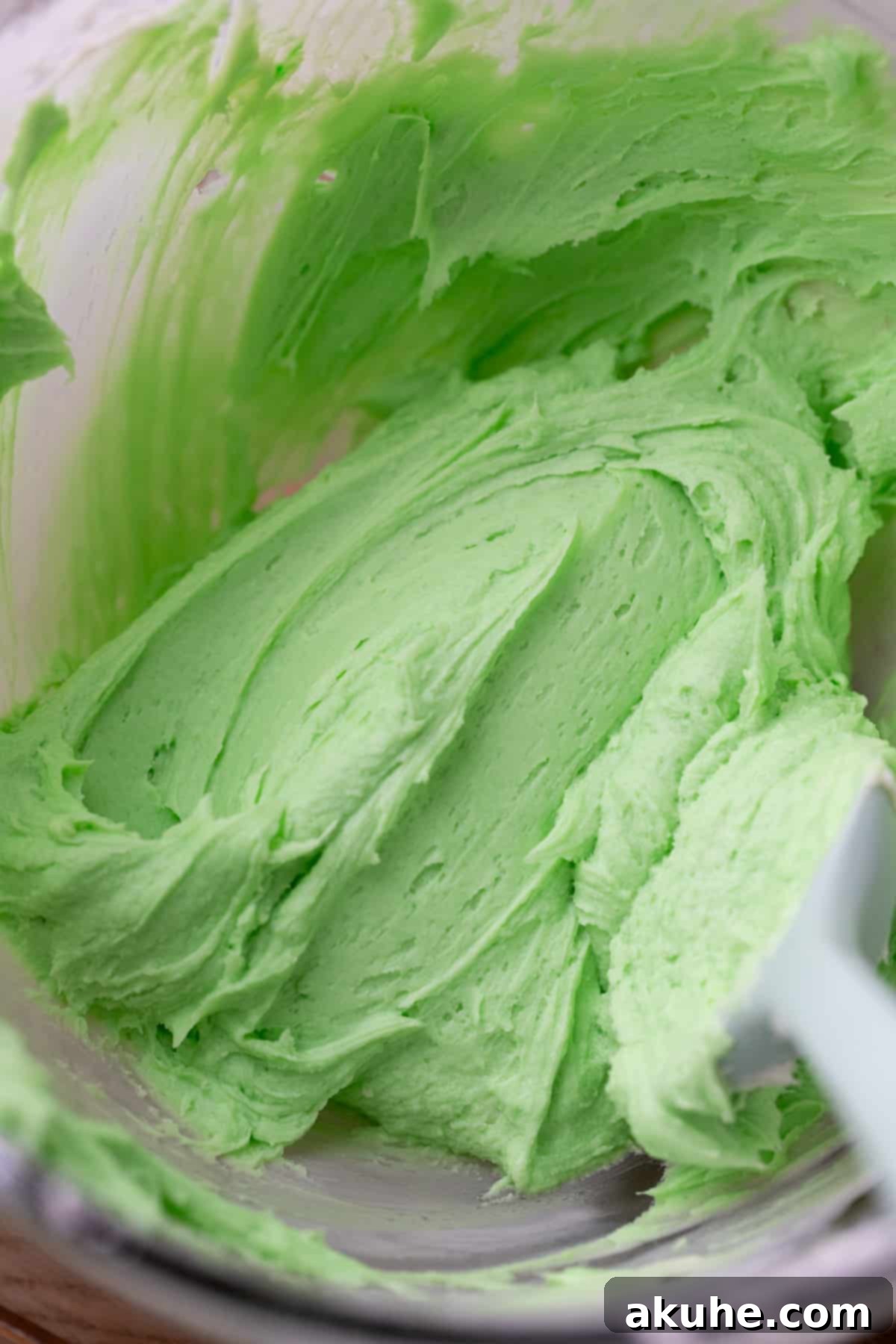 Grinchy Holiday Cake 6 Smooth, vibrant green cream cheese frosting in a clear glass bowl, ready to be spread onto the Grinch cake.