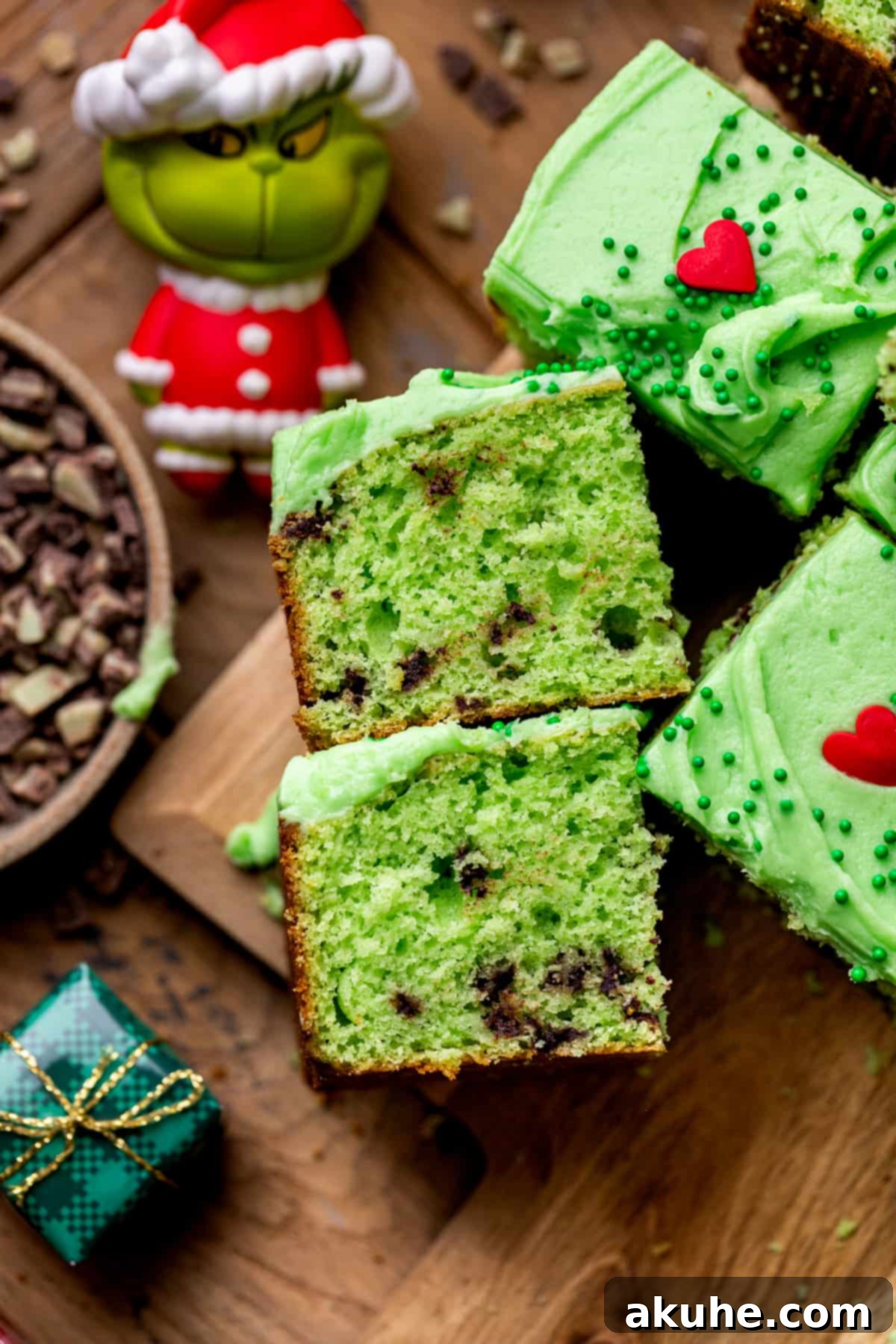 Grinchy Holiday Cake 8 Two slices of vibrant green Grinch cake, showcasing the moist texture, mint pieces, and creamy green frosting with red heart sprinkles.