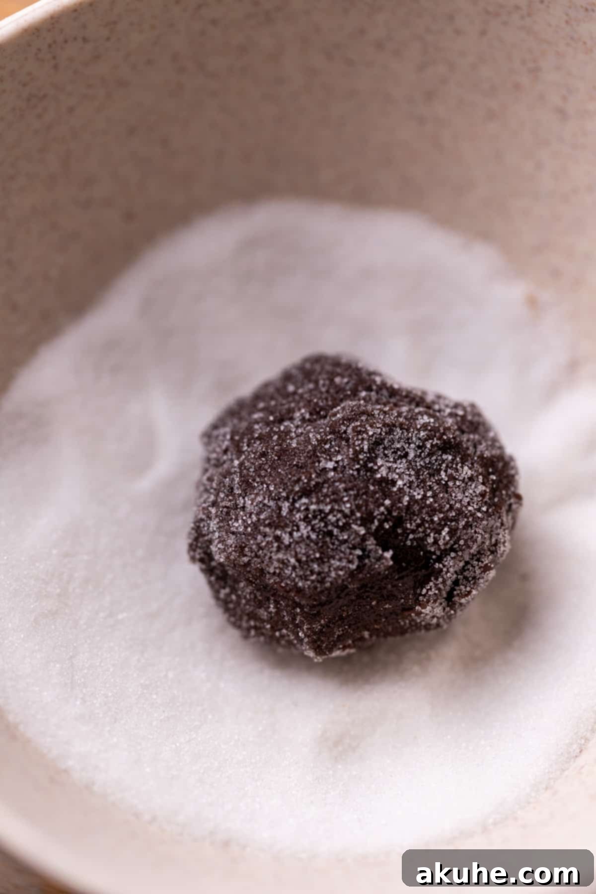 A ball of chocolate cookie dough, freshly rolled in granulated sugar.