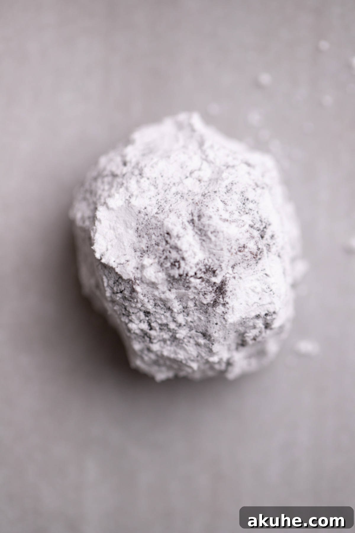 A powdered sugar-coated chocolate cookie dough ball placed on a parchment-lined cookie sheet.