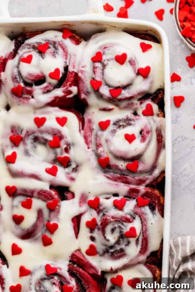Vibrant red velvet cinnamon rolls topped with creamy white cream cheese frosting and festive red heart sprinkles.