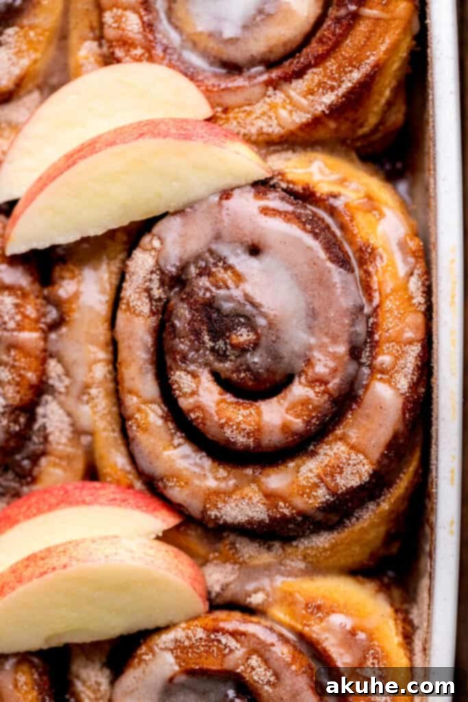 A close-up of a warm apple cinnamon roll, beautifully revealing its spiced apple filling swirled within the tender dough and sweet glaze.