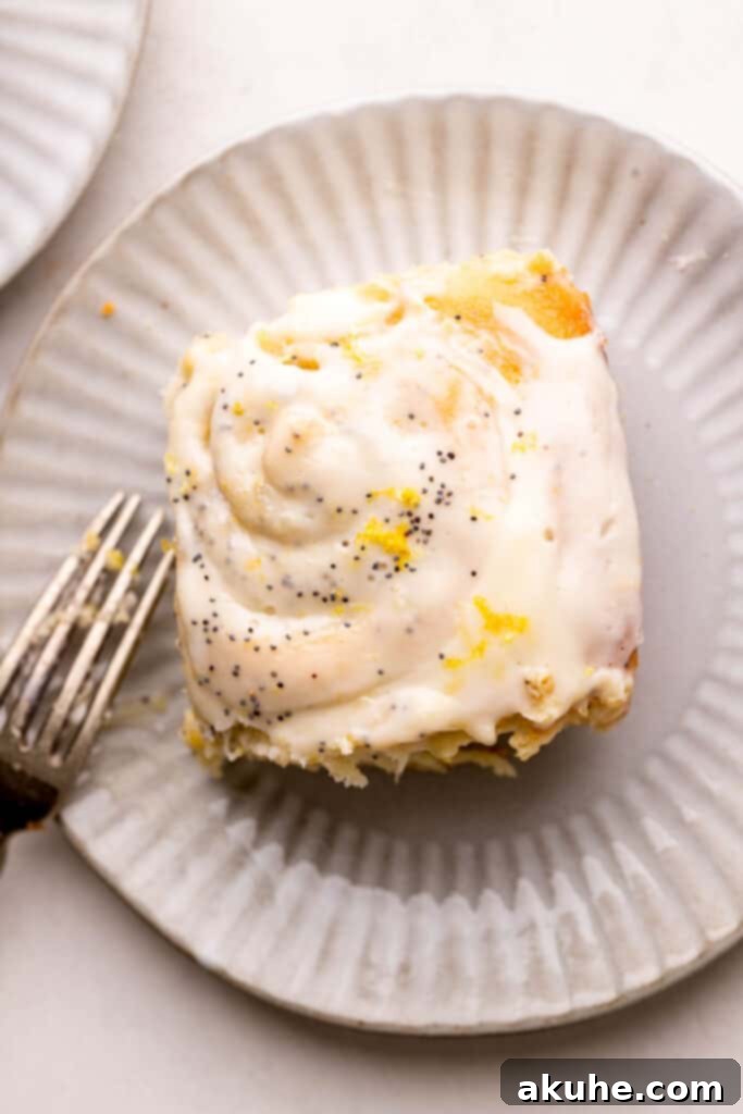 A single zesty lemon roll, generously drizzled with a bright white lemon glaze, beautifully plated and ready to be enjoyed.