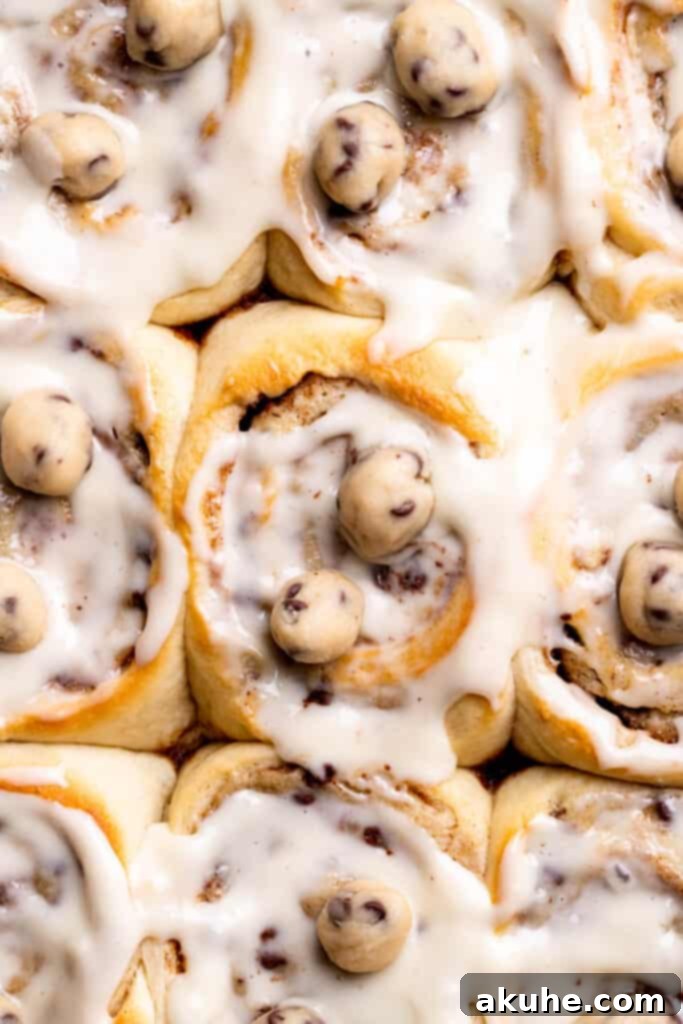 A close-up of incredibly gooey cookie dough cinnamon rolls, showing melted cookie dough chunks within the cinnamon swirl.