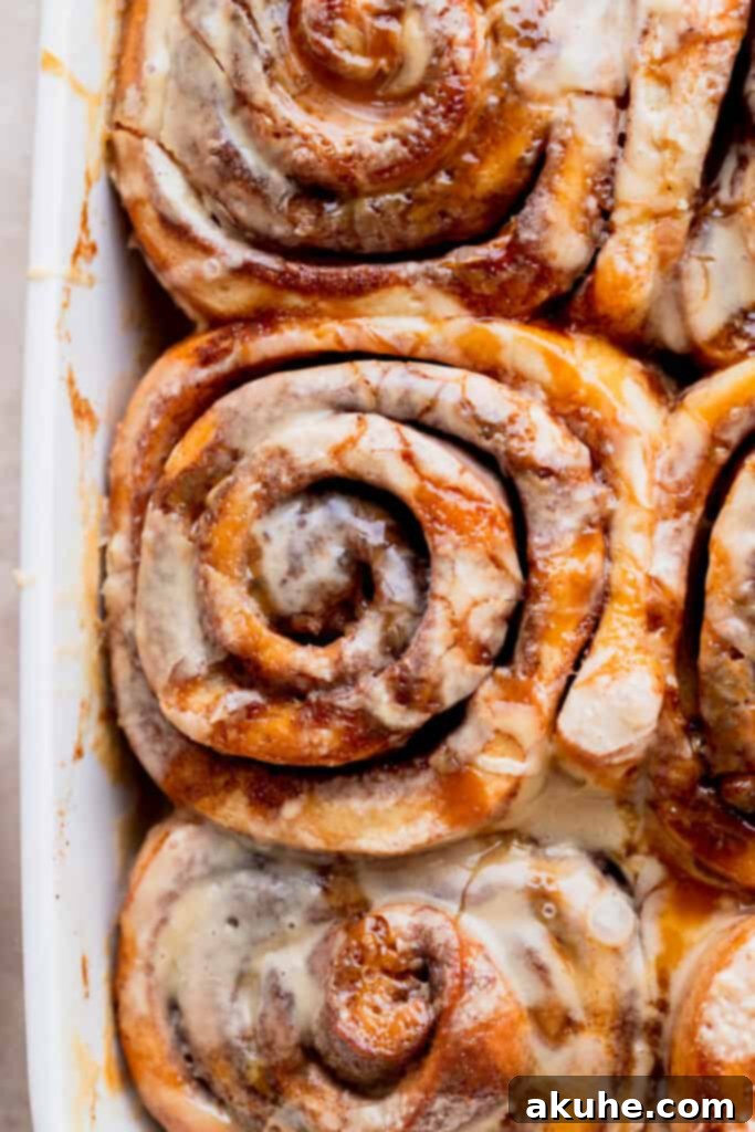 A close-up of a perfectly baked caramel cinnamon roll nestled in a baking pan, showing its rich, glistening golden caramel topping.