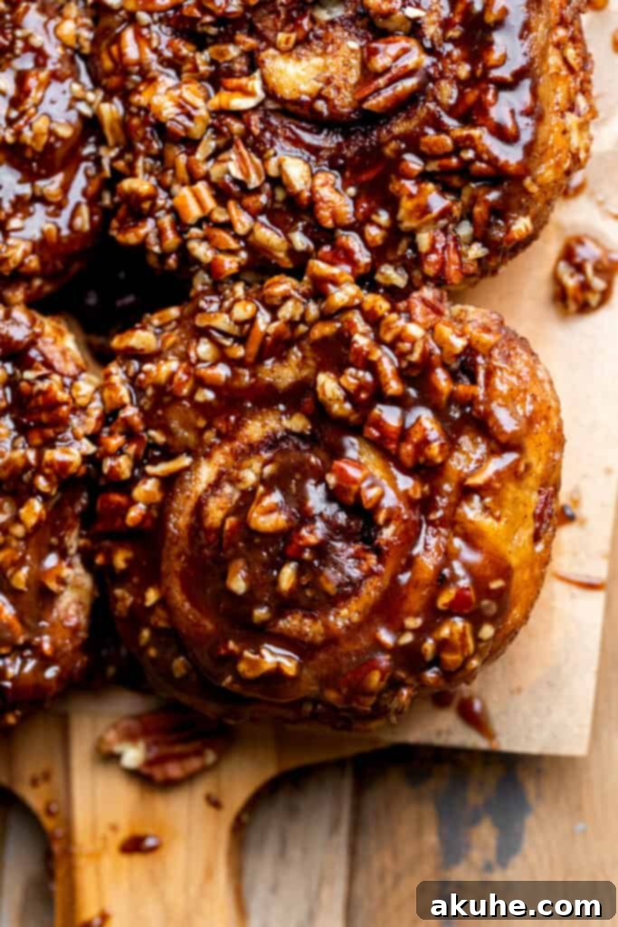 A close-up view of warm, glistening sticky buns, richly topped with caramelized maple pecan, fresh from the oven.