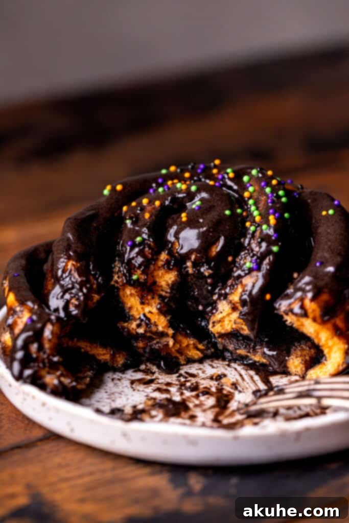 A Halloween-themed cinnamon roll with vibrant orange dough and striking black cocoa frosting, with a playful bite taken out.
