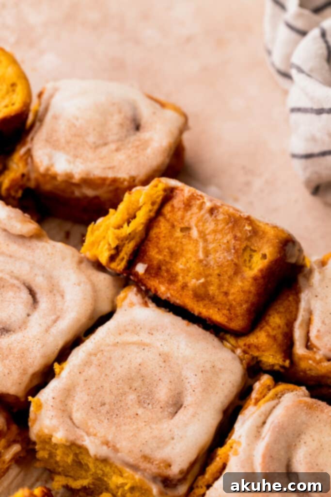 A single, perfectly baked pumpkin spice cinnamon roll, generously frosted with cream cheese icing and dusted with aromatic cinnamon.