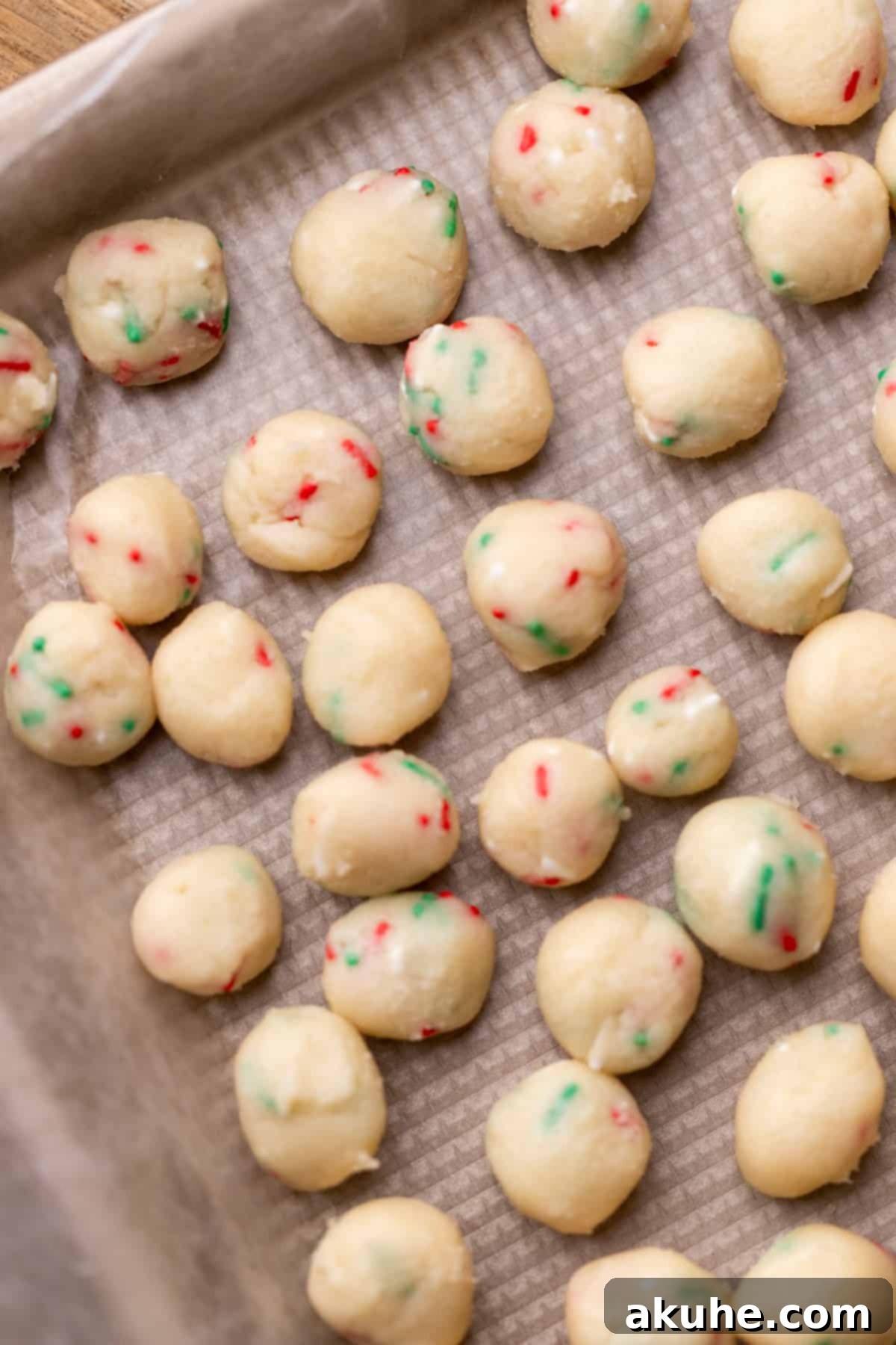 Sugar Cookie Dream Cheesecake 7 Numerous small, edible sugar cookie dough balls, dotted with festive sprinkles, neatly arranged on a wax paper-lined cookie sheet.