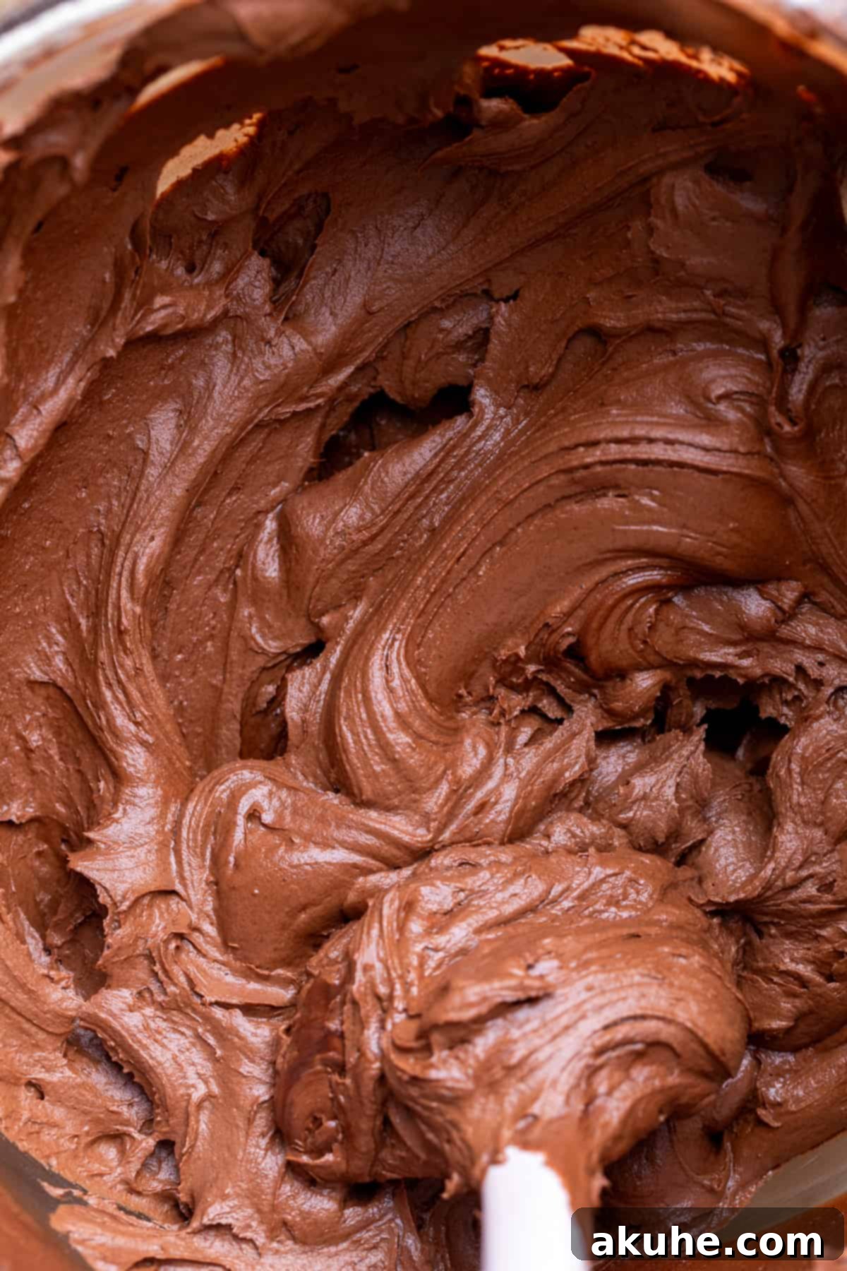 Luxurious chocolate frosting filling a glass bowl, showcasing its smooth and creamy texture.