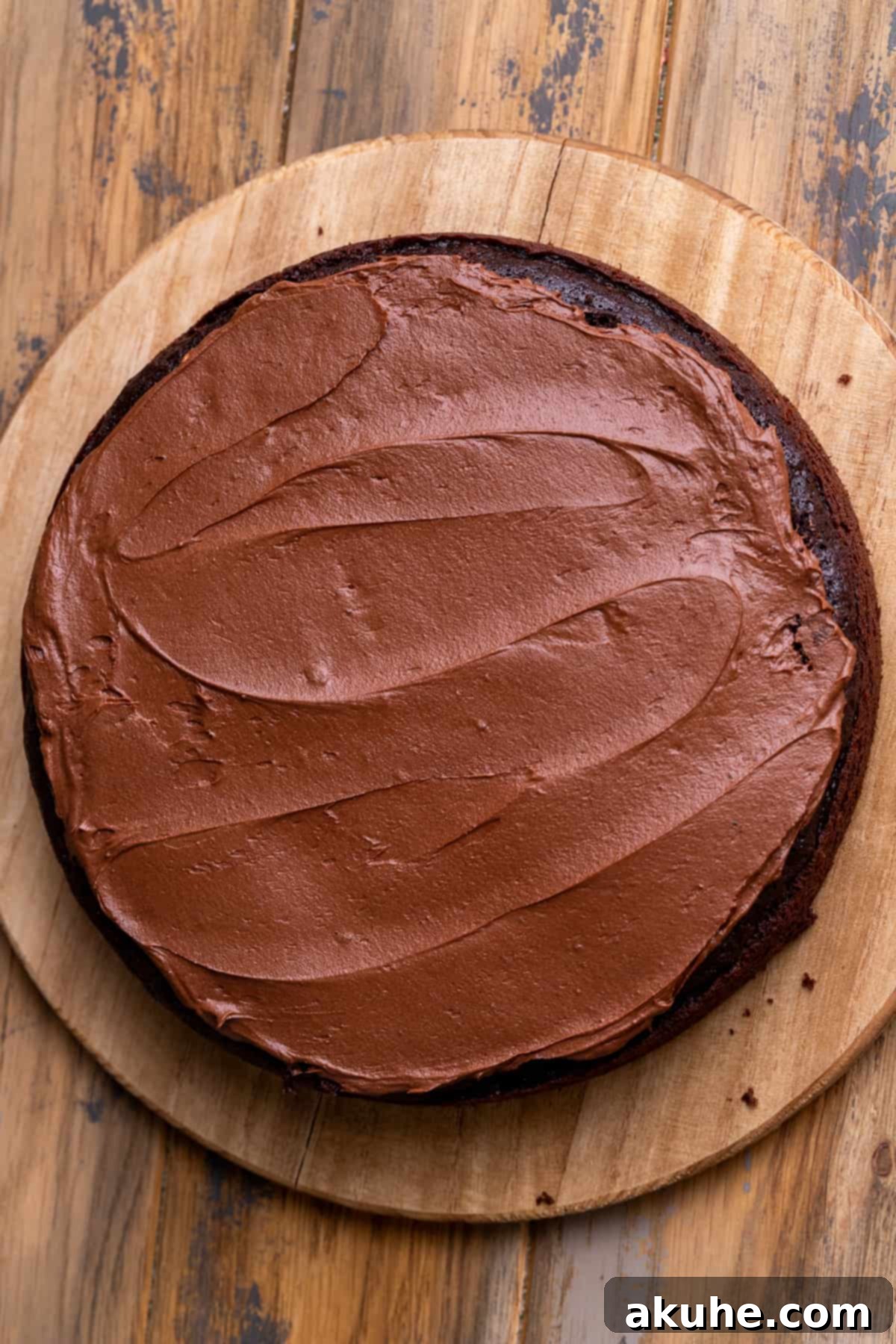A chocolate cake layer generously covered with smooth chocolate frosting, ready for the next layer.