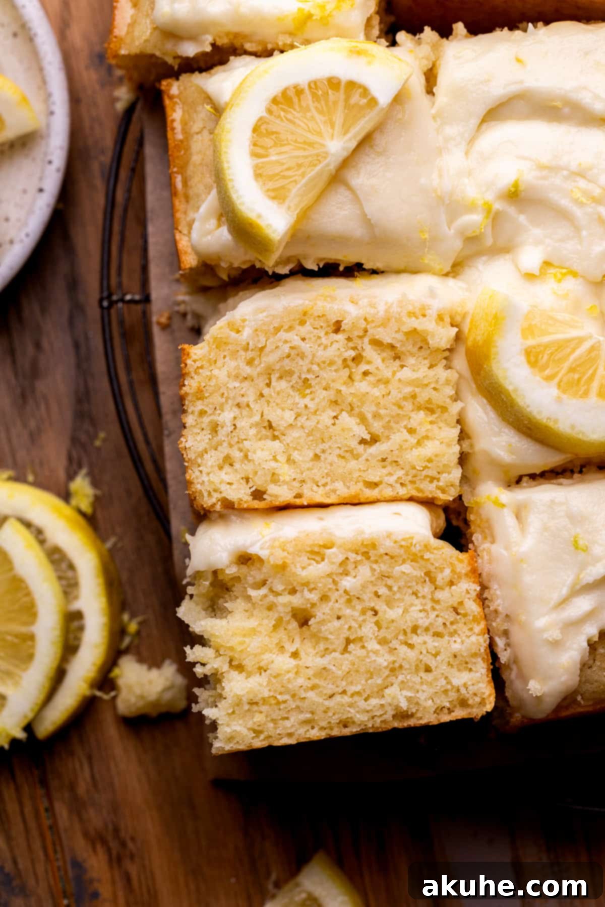A perfectly cut slice of lemon drizzle cake, showing off its moist texture and thick layer of lemon cream cheese frosting.