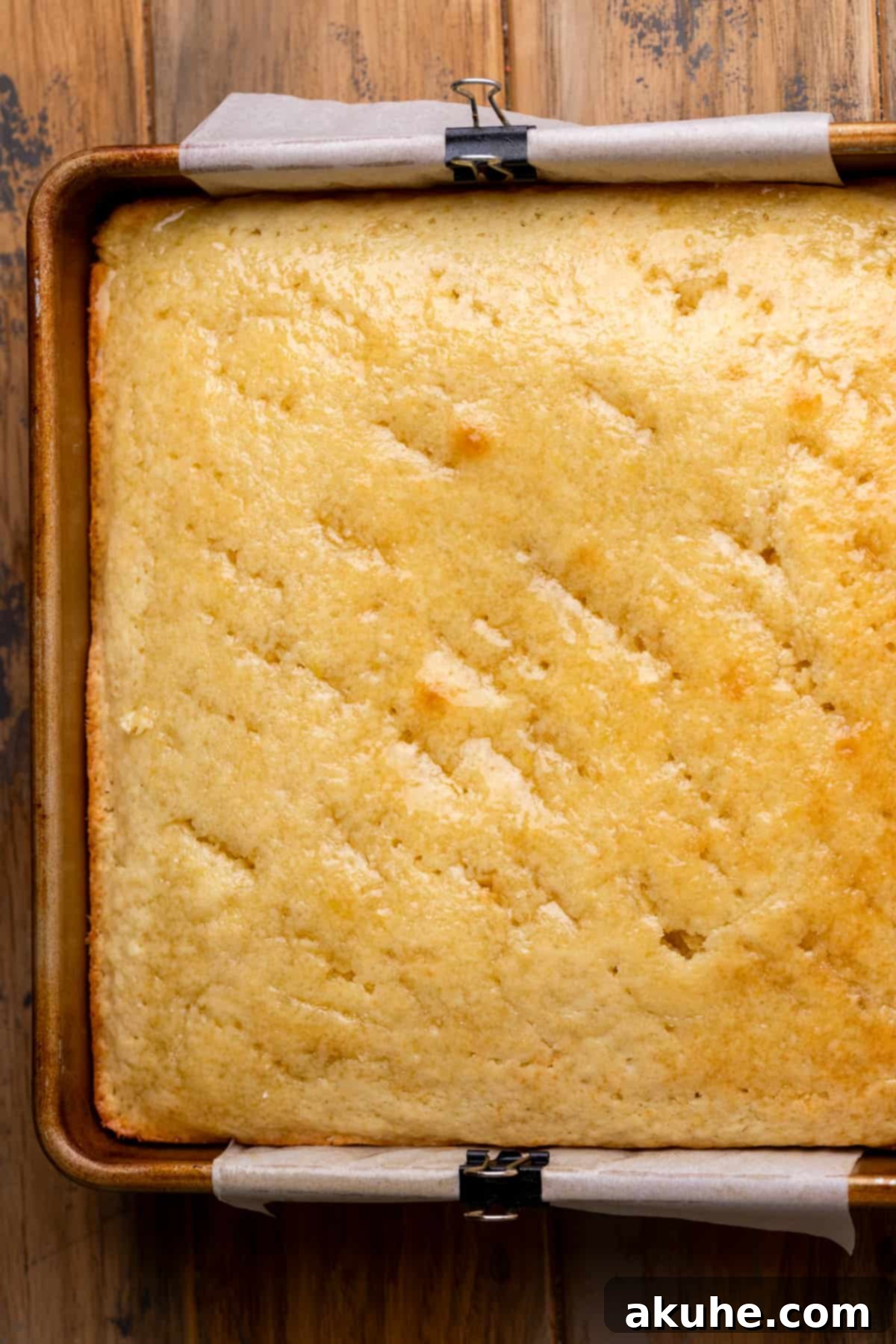 A baked lemon cake with a fork used to poke holes, ready for the drizzle to be poured over.