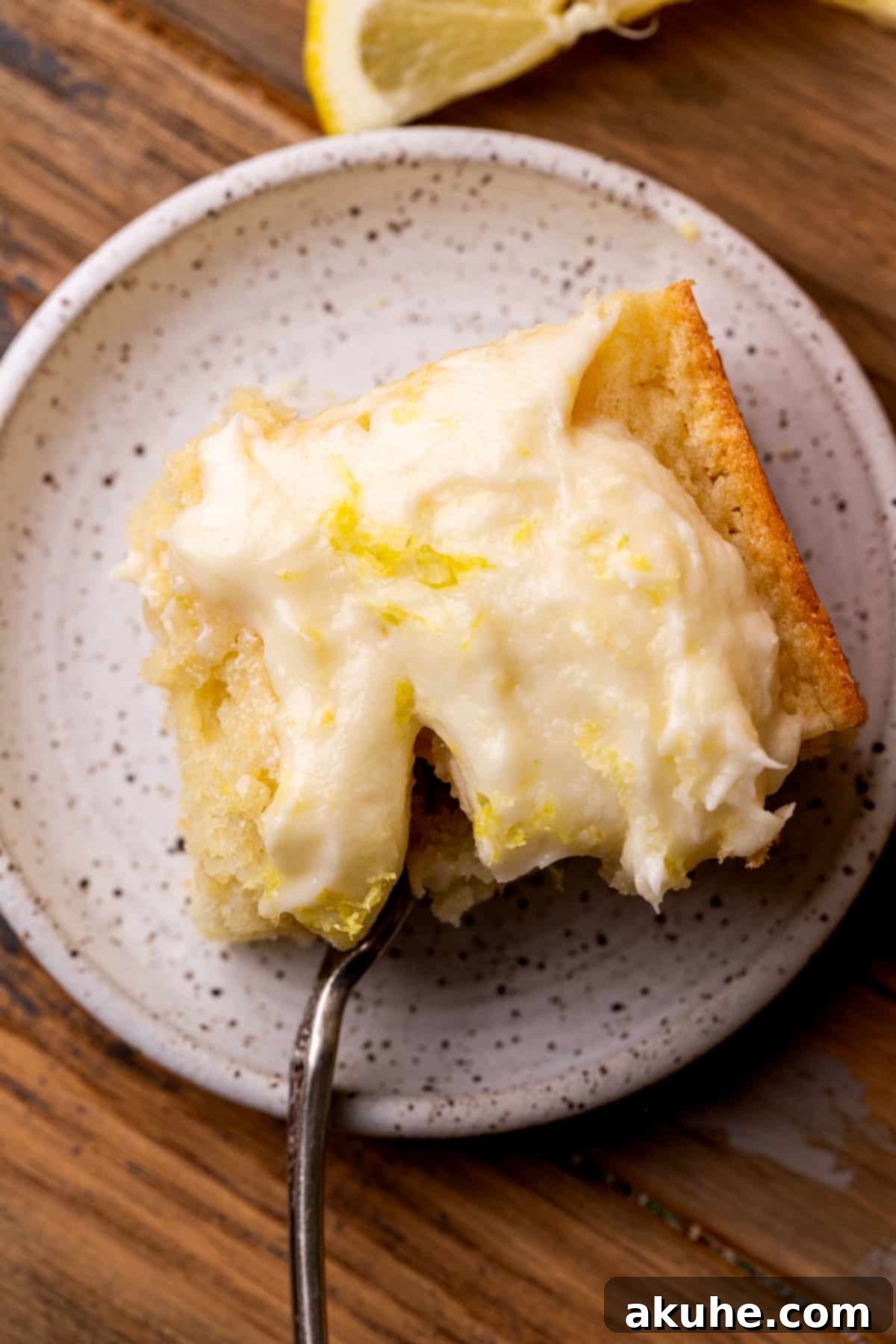 A beautiful slice of lemon drizzle cake, with a fork inserted, ready for a delightful taste.