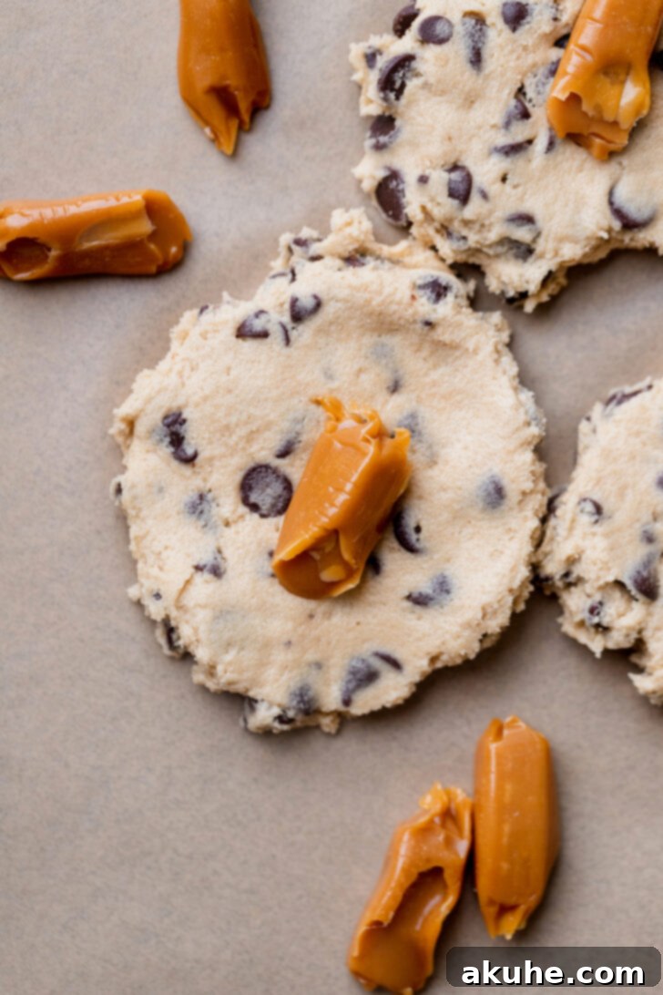 Gooey Caramel Chocolate Chip Cookies 6 A cookie dough ball with a soft caramel piece being carefully placed into its center, ready for stuffing.