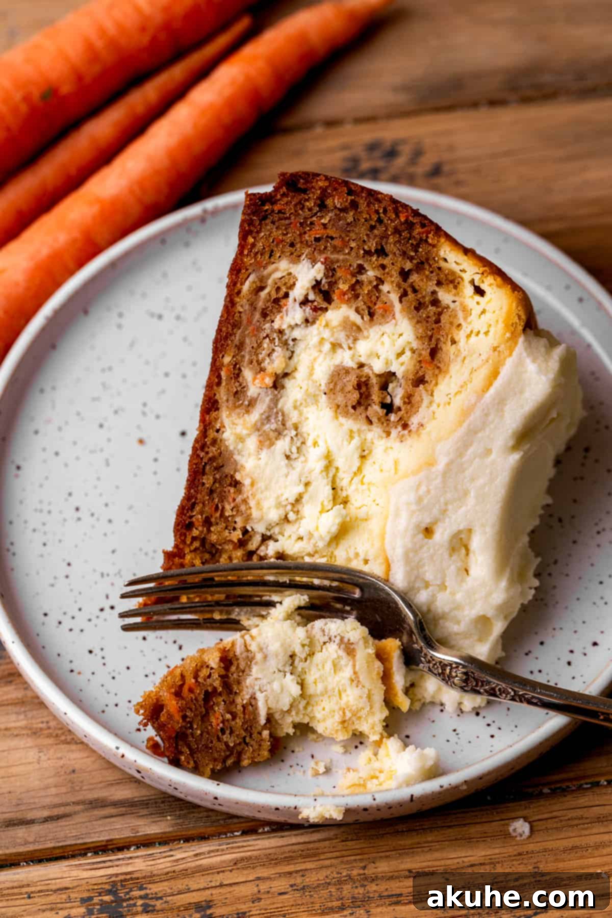 Carrot Cake Swirl Cheesecake 11 A delightful slice of carrot cake cheesecake on a plate with a fork, ready to be enjoyed.