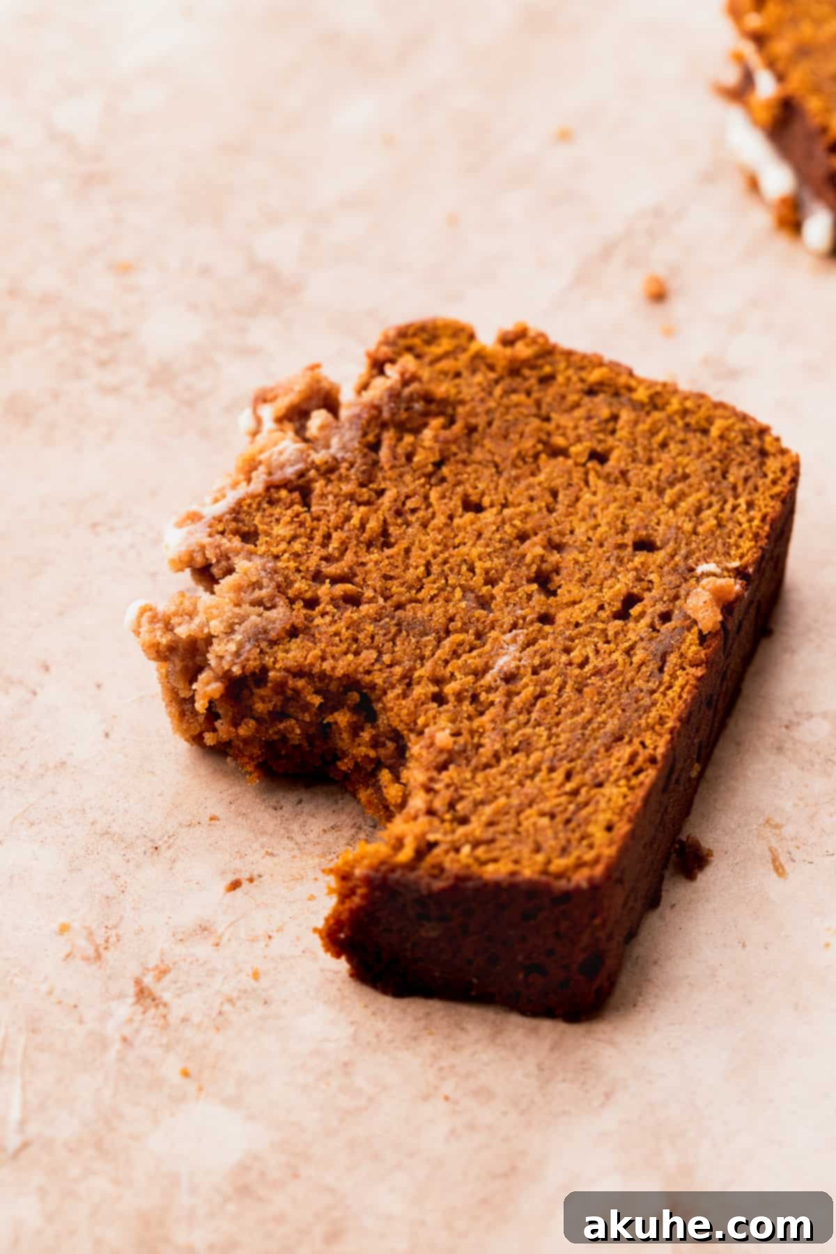 Spiced Pumpkin Loaf with Cream Cheese Frosting 3 A slice of pumpkin bread with cream cheese frosting, showing a bite taken out, on a white plate.