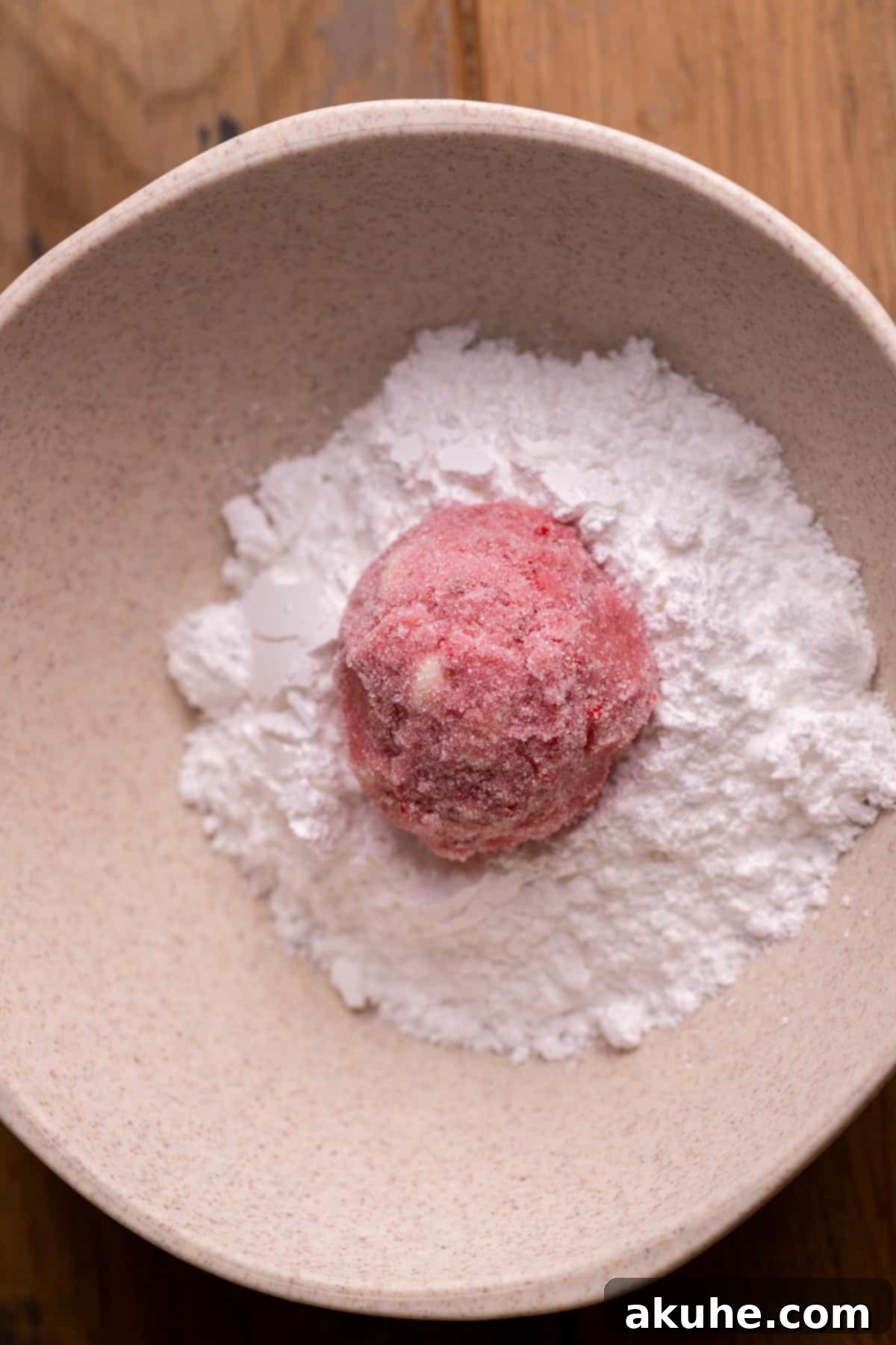 Pink Strawberry Crinkle Delights 7 Cookie dough ball being rolled in powdered sugar for the final coating.