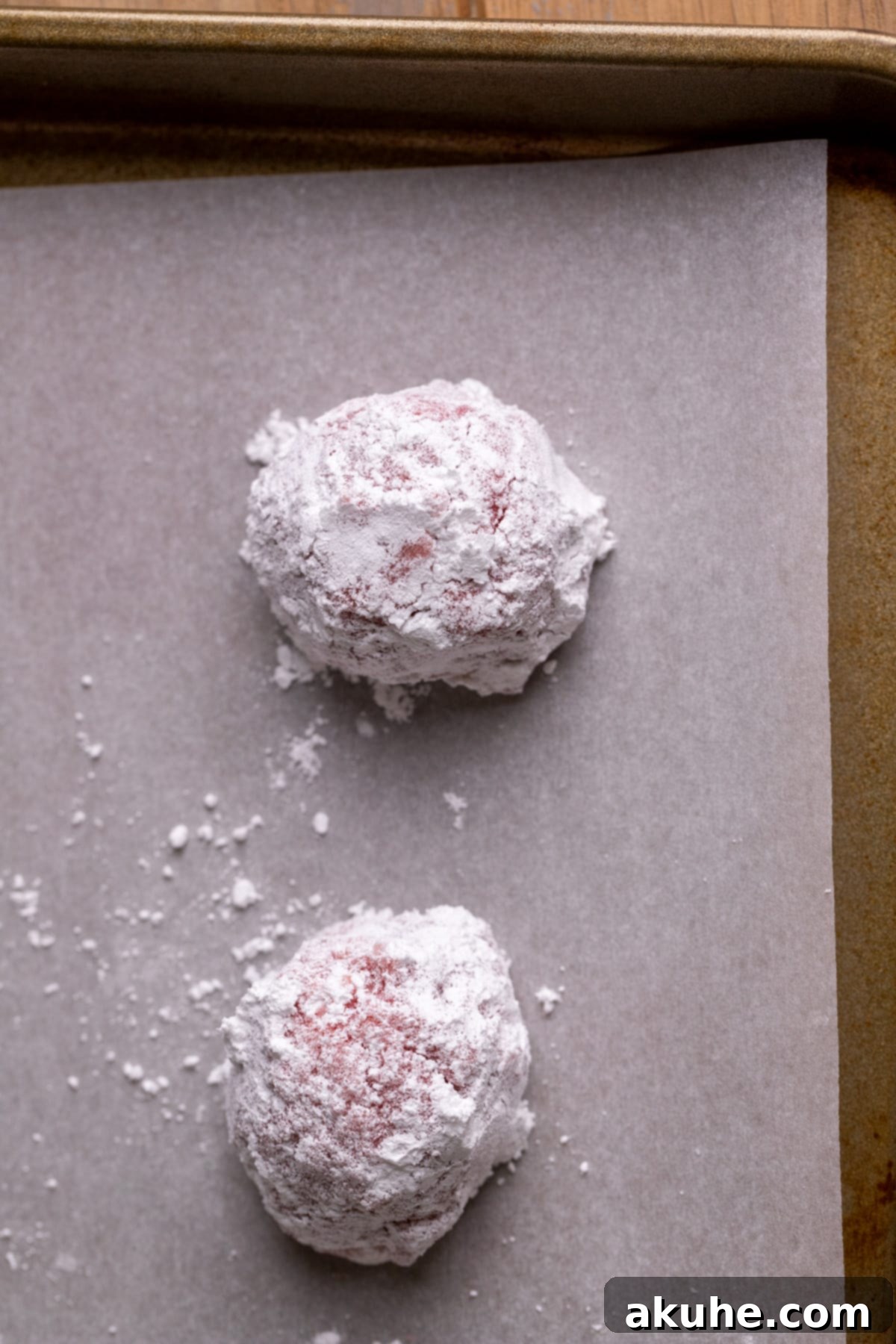 Pink Strawberry Crinkle Delights 8 Cookie dough balls rolled in powdered sugar, arranged on a parchment-lined cookie sheet, ready for baking.