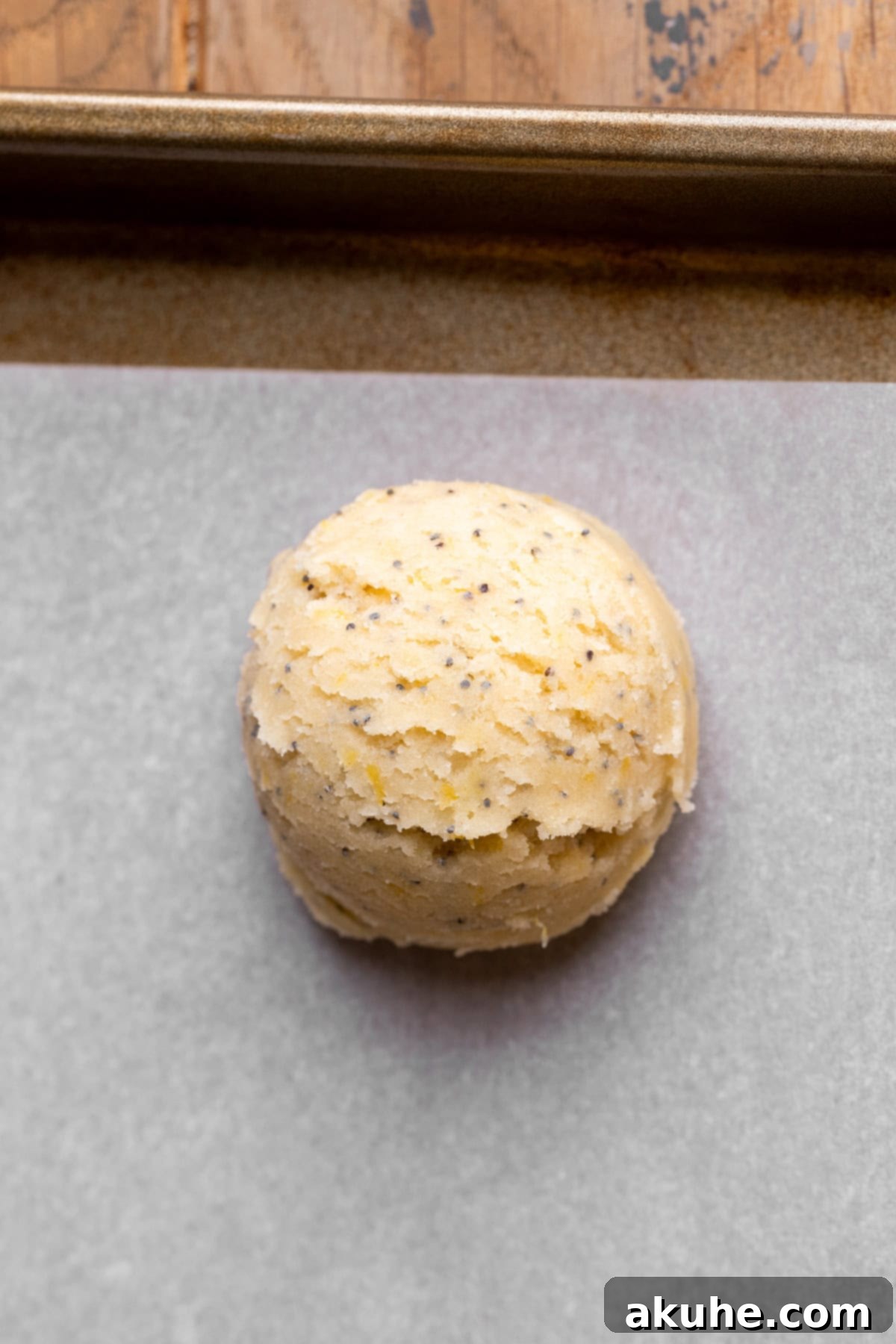 Zesty Lemon Poppy Seed Cookies 8 A perfectly formed cookie dough ball with hidden cheesecake filling, placed on a cookie sheet.