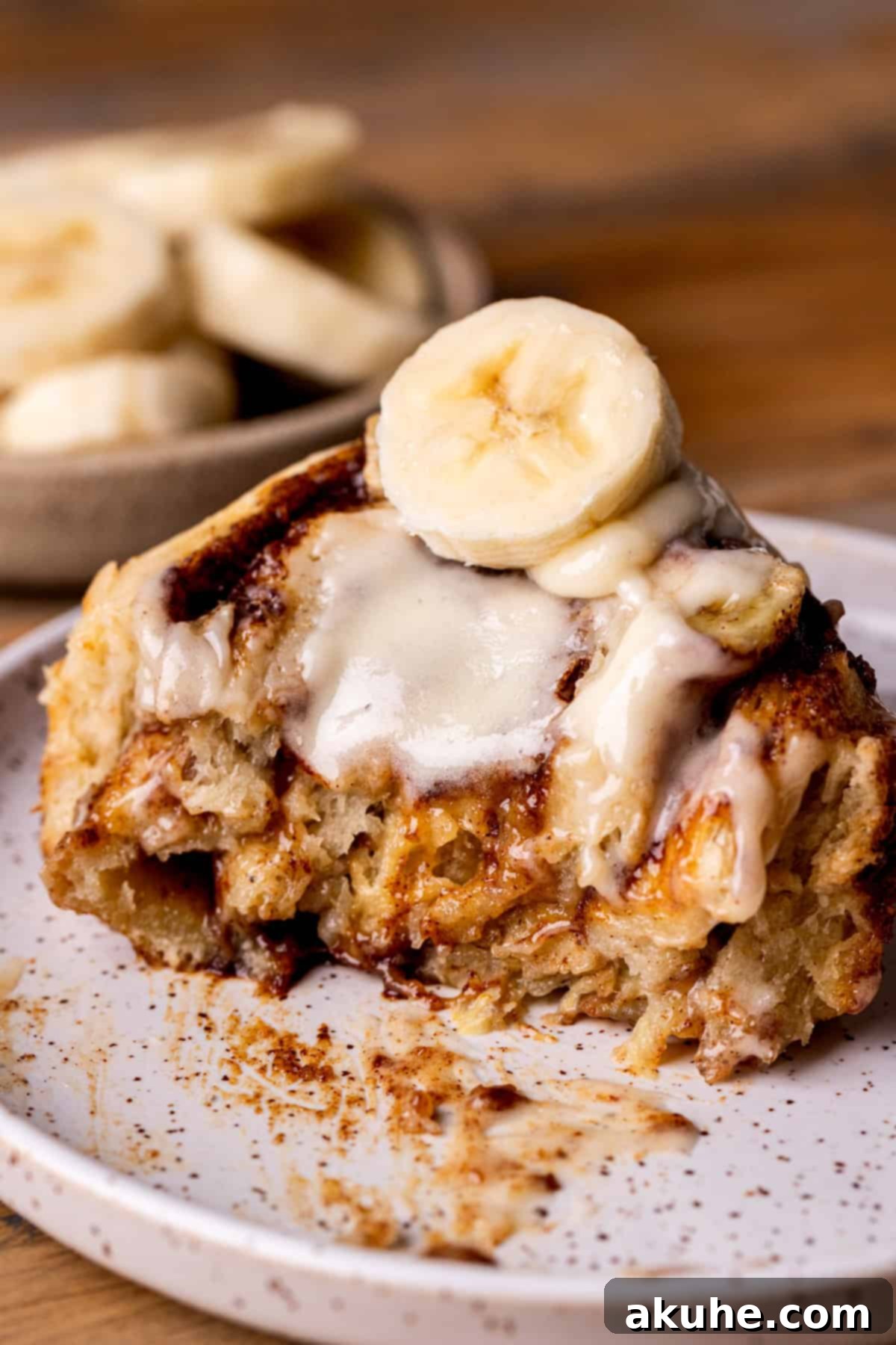 Banana Swirl Buns 3 A banana cinnamon roll on a plate with a bite taken out, showing the gooey center.