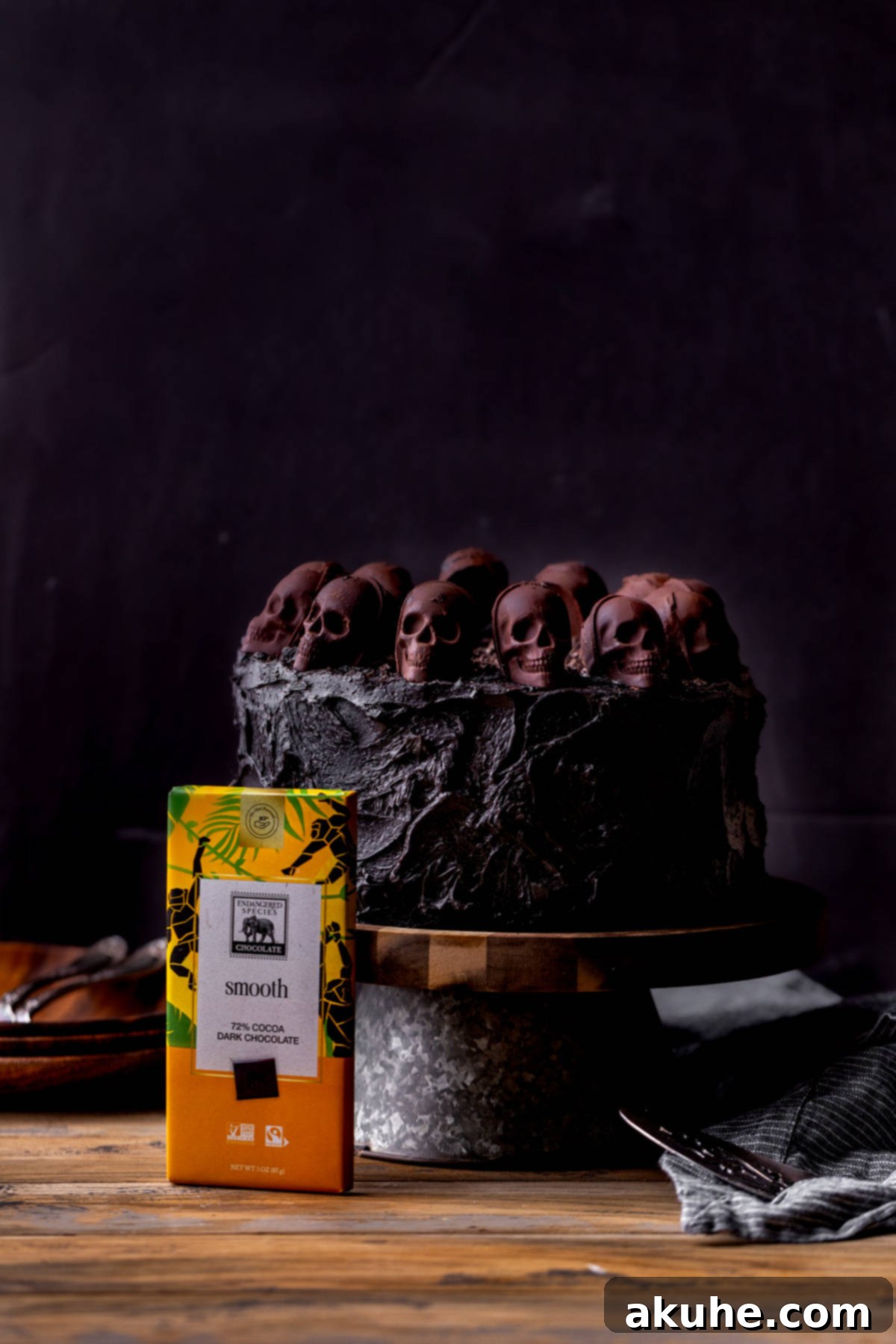 Bewitching Halloween Chocolate Cake 3 A beautifully decorated black velvet chocolate cake, featuring intricate chocolate skull designs, presented on a minimalist cake stand.