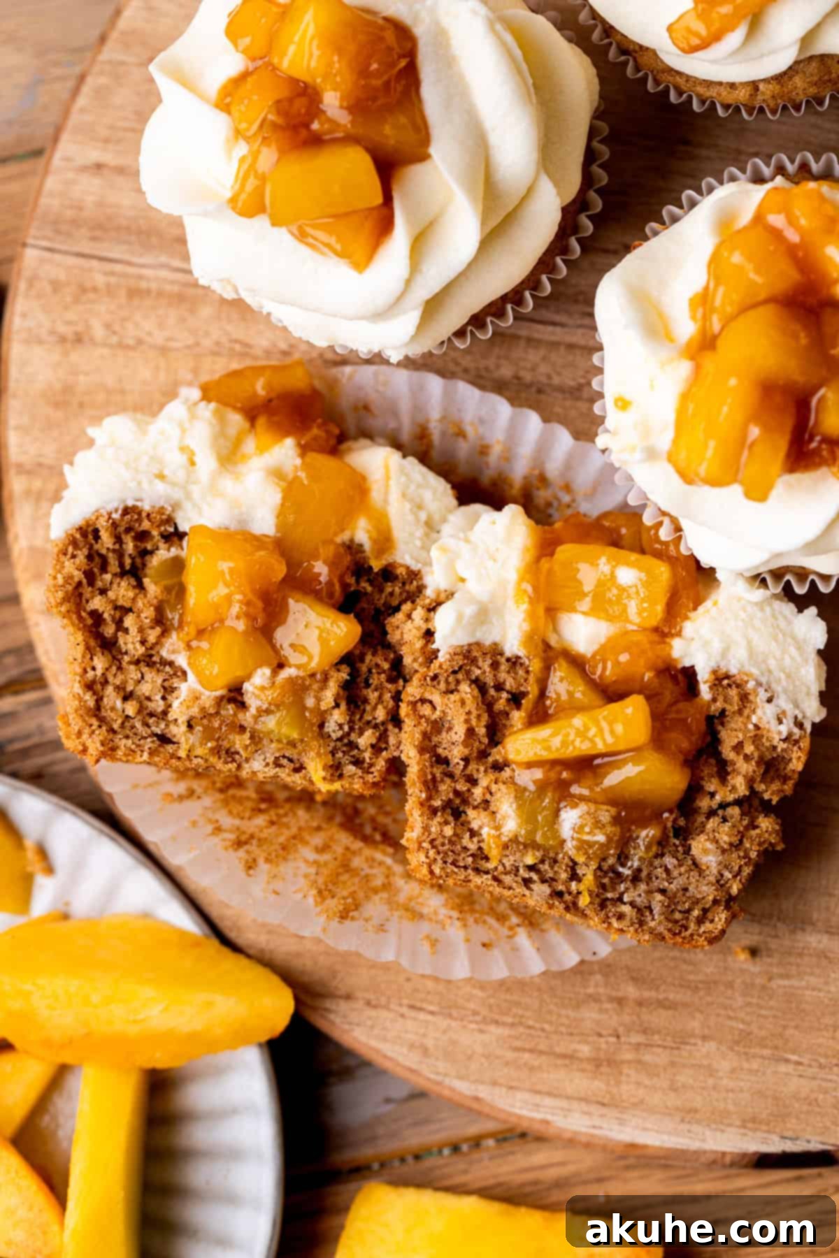 One cinnamon peach cupcake cut in half, showcasing the layers of cake, peach filling, and frosting.
