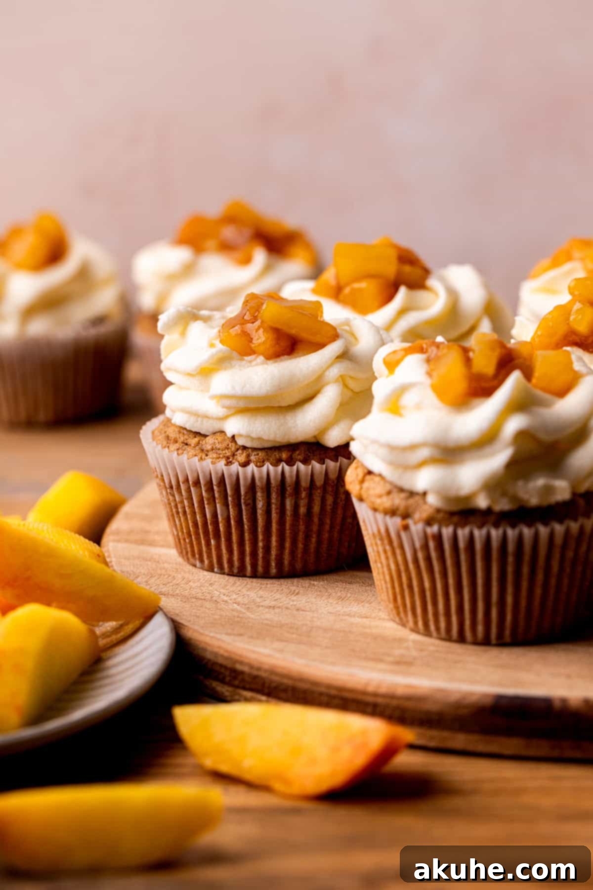 A collection of beautifully frosted cinnamon peach cupcakes on a rustic wood board.