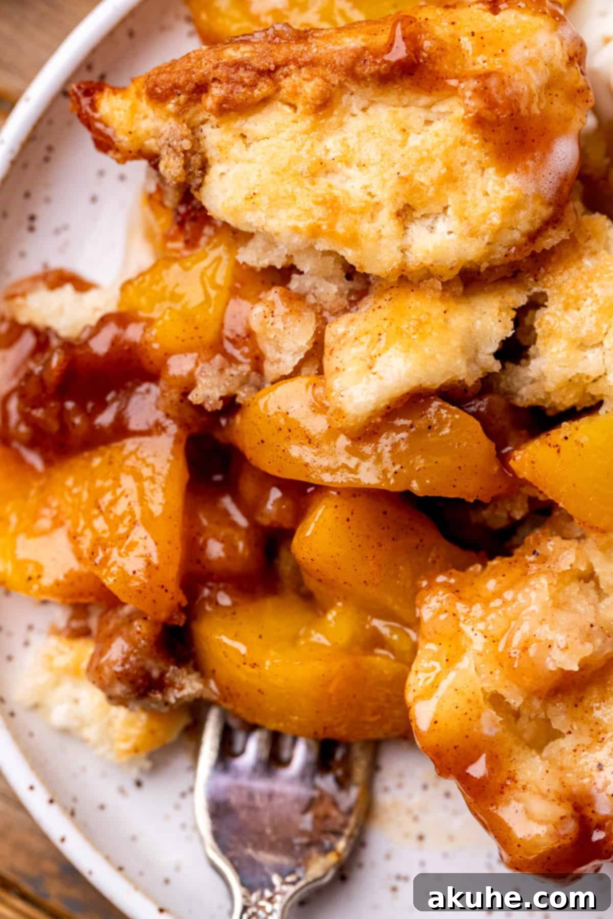 A slice of warm cinnamon peach cobbler on a white plate, showcasing the golden biscuit topping and peachy filling.